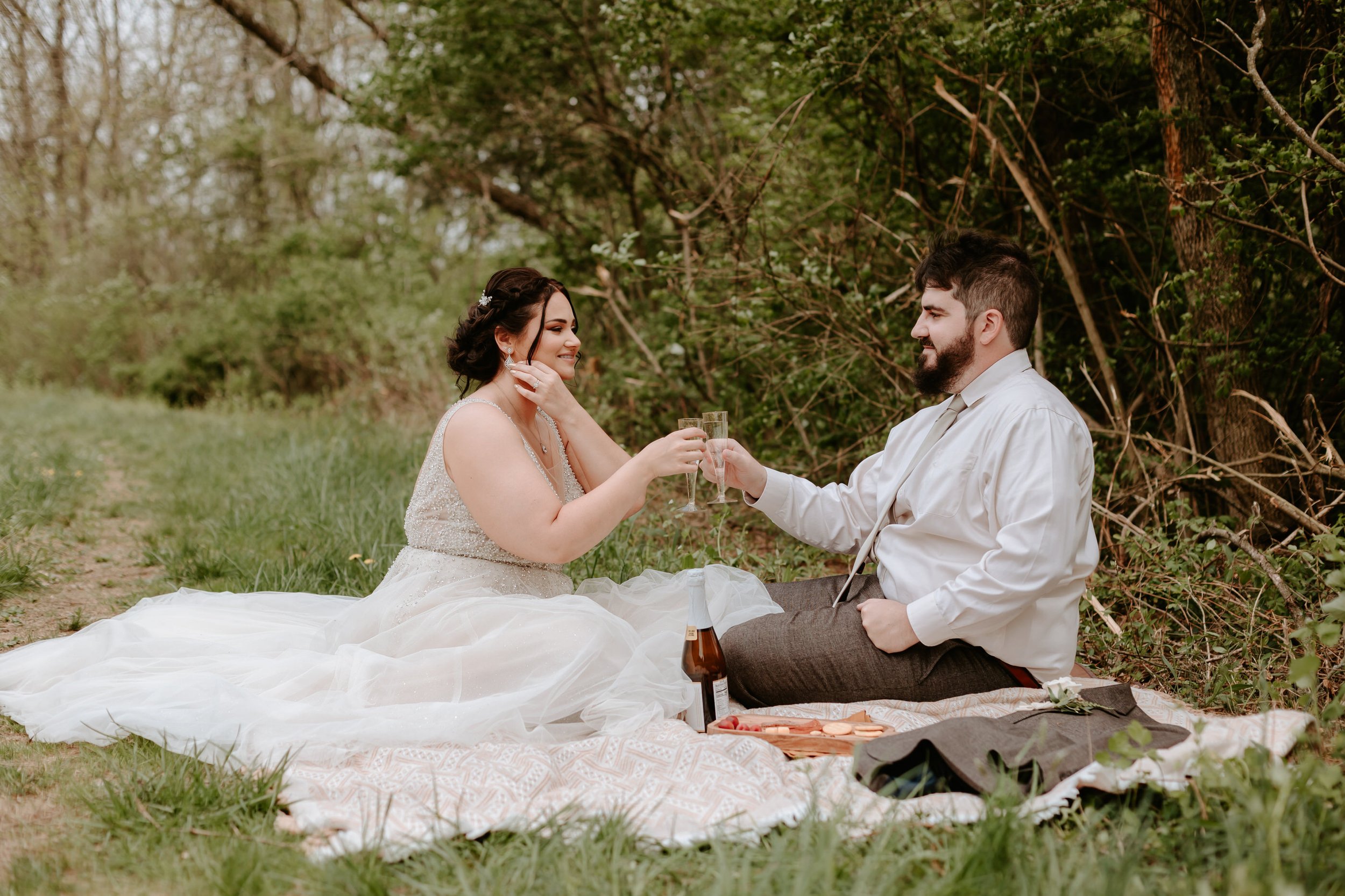 Couple sits on blanket and share a champagne toast.