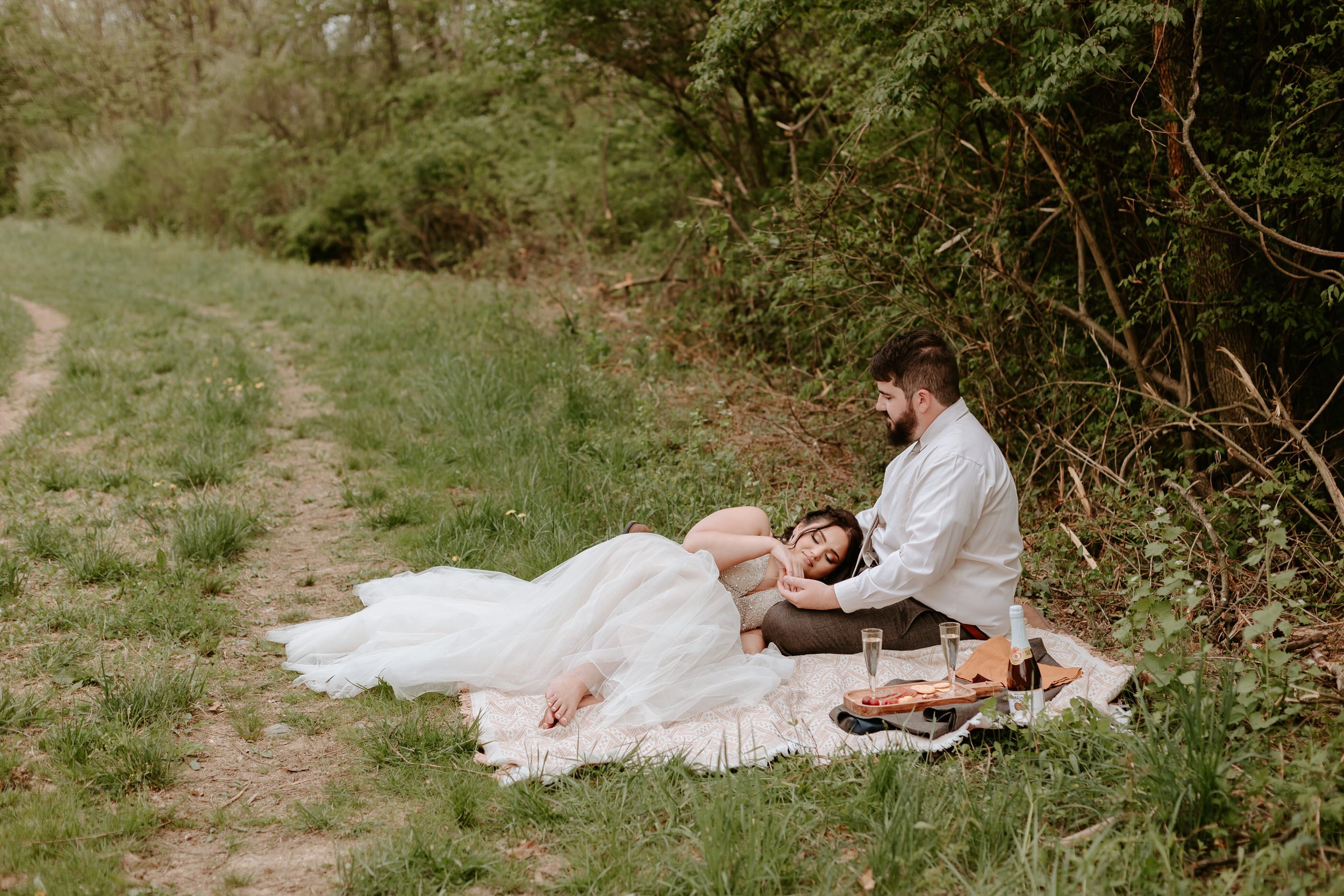 Bride lays on grooms lap during a picnic.