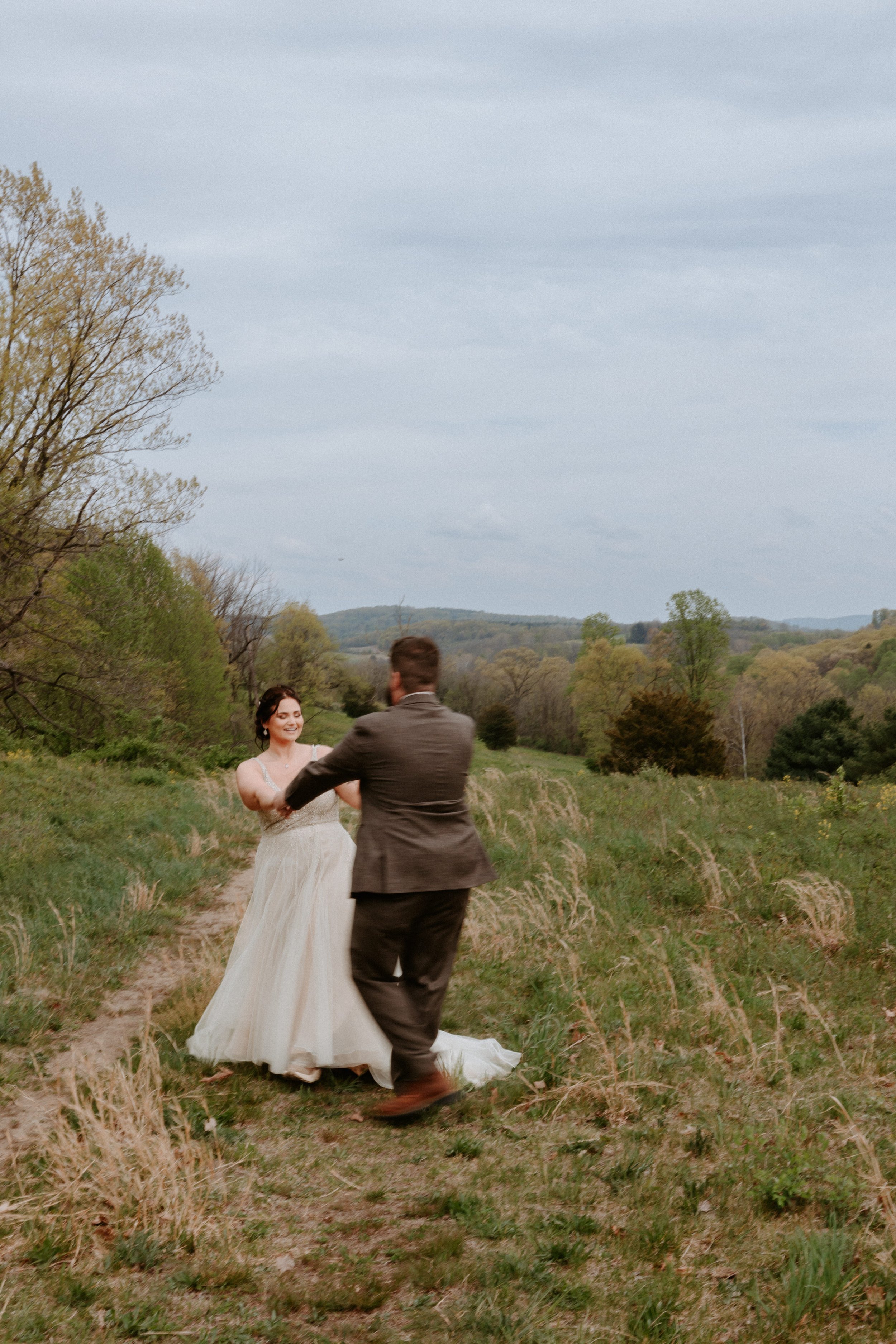 Bride and groom spin in circles in open landscape.