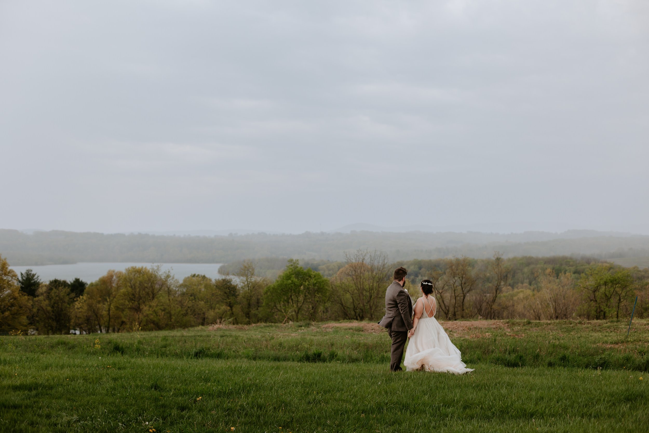 Man and woman in wedding attire look out over open landscape.