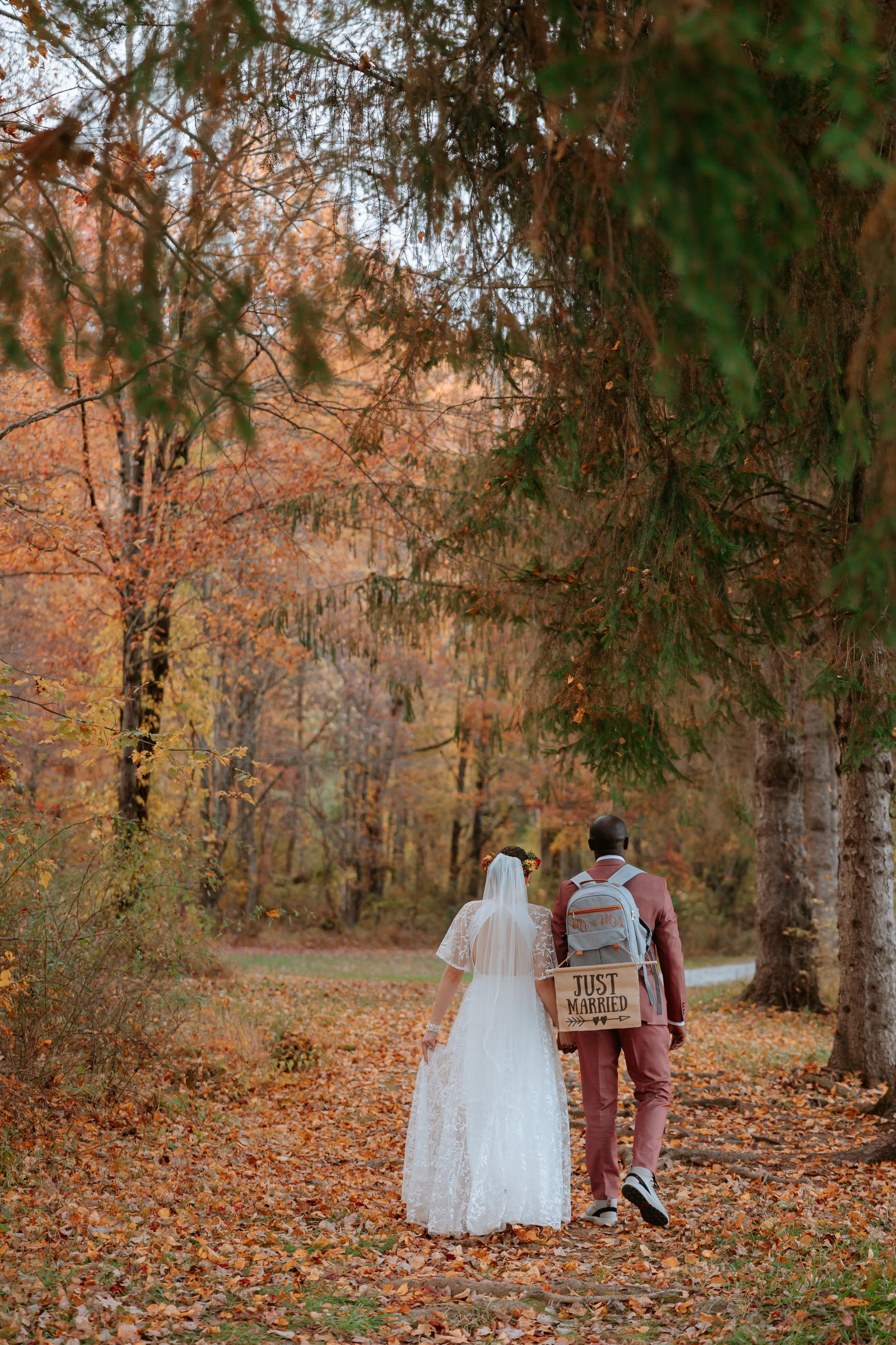 A bride and groom walking through the woods with their backpacks.