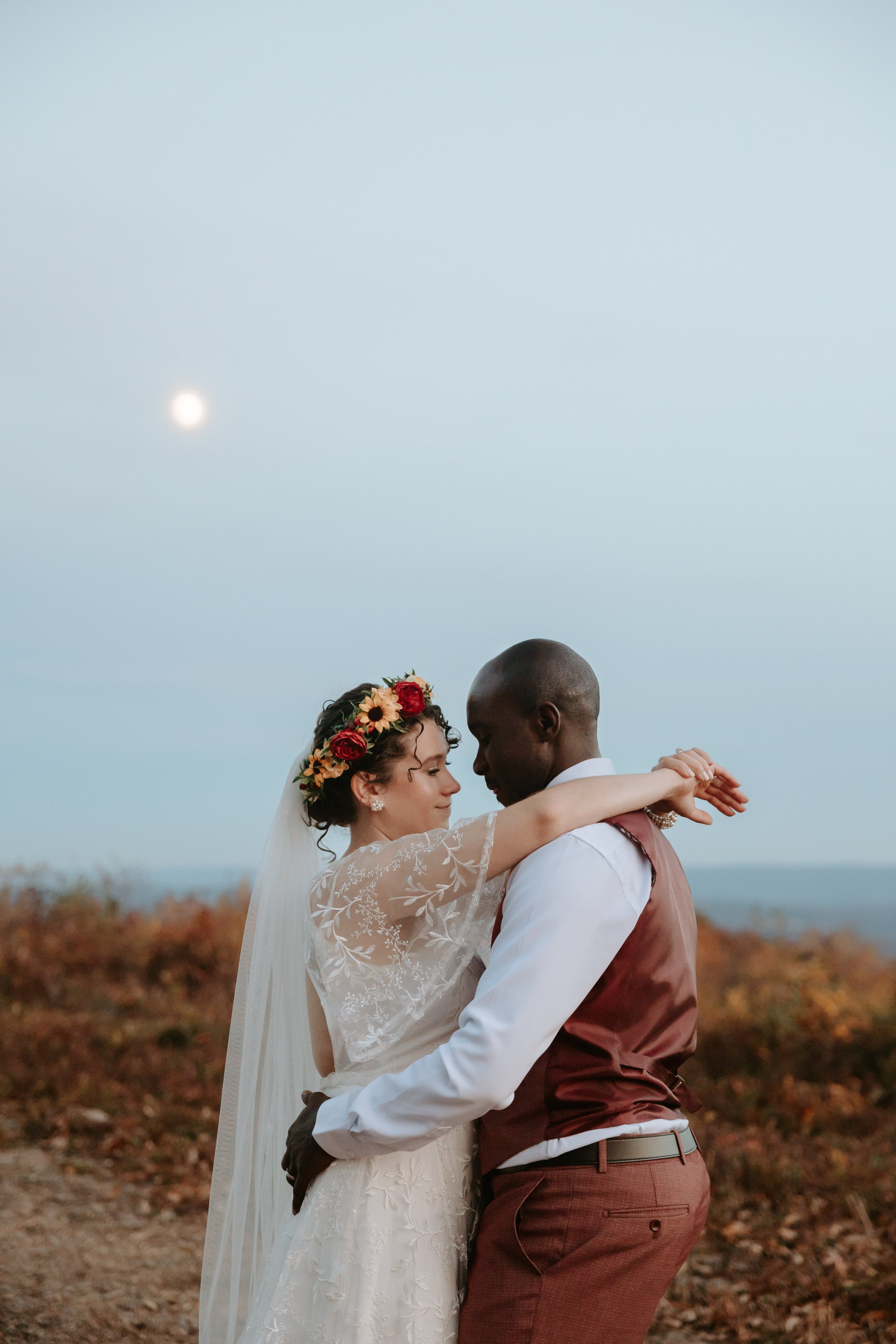 A bride and groom embrace in front of a full moon.