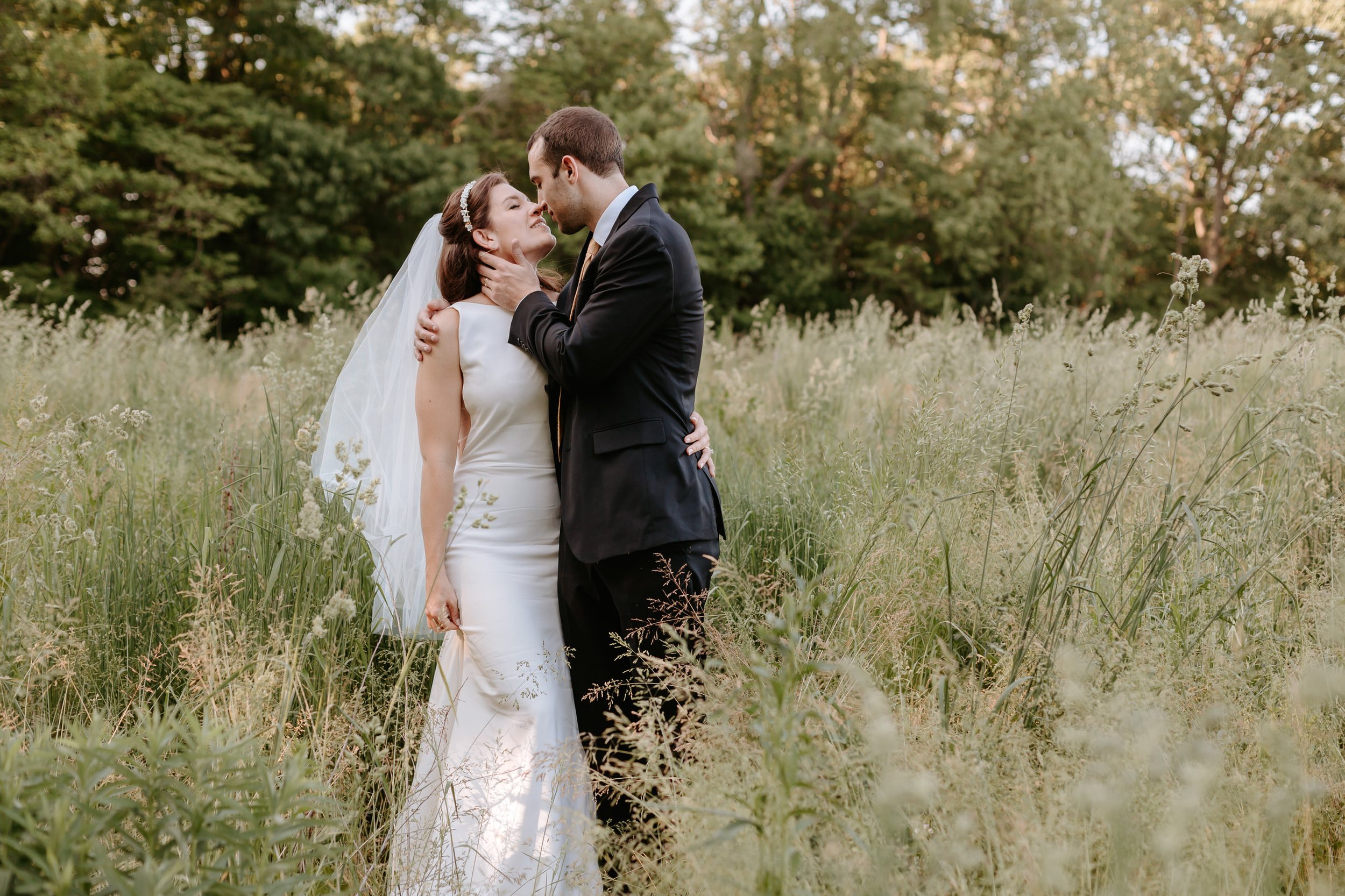 A bride and groom kissing in a field of tall grass.