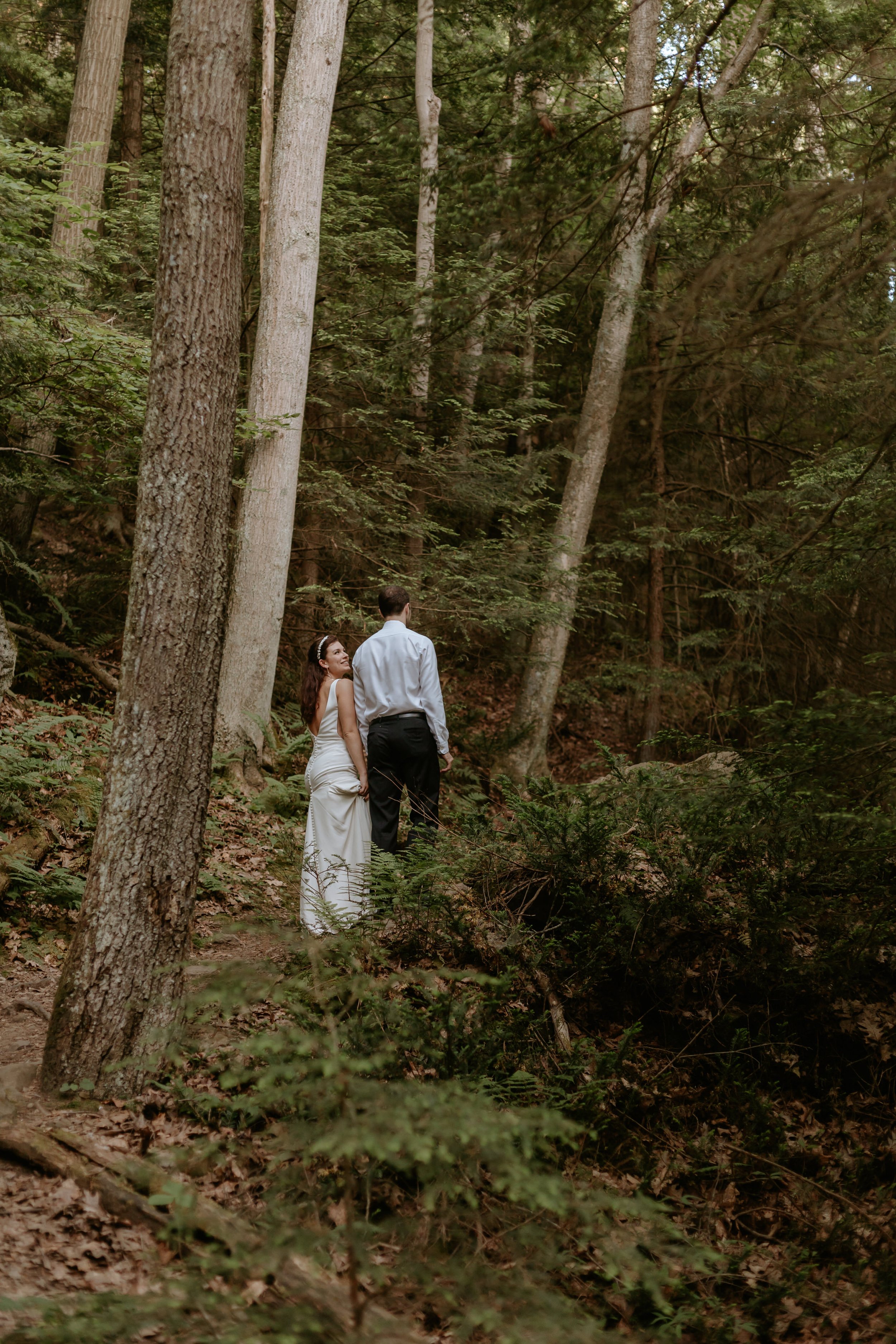 Bride and groom walking in forest together.
