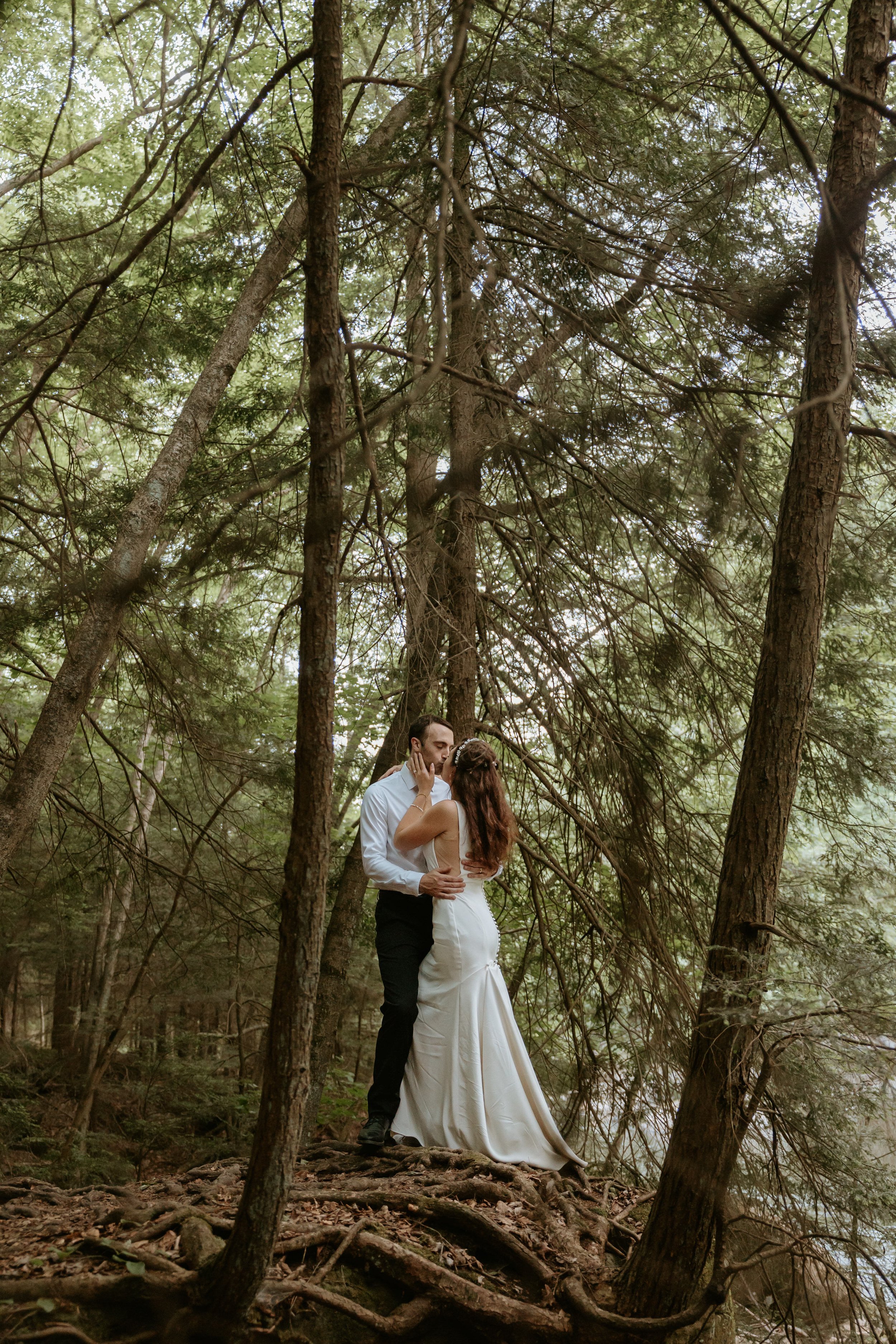 Bride and groom embrace in forest.