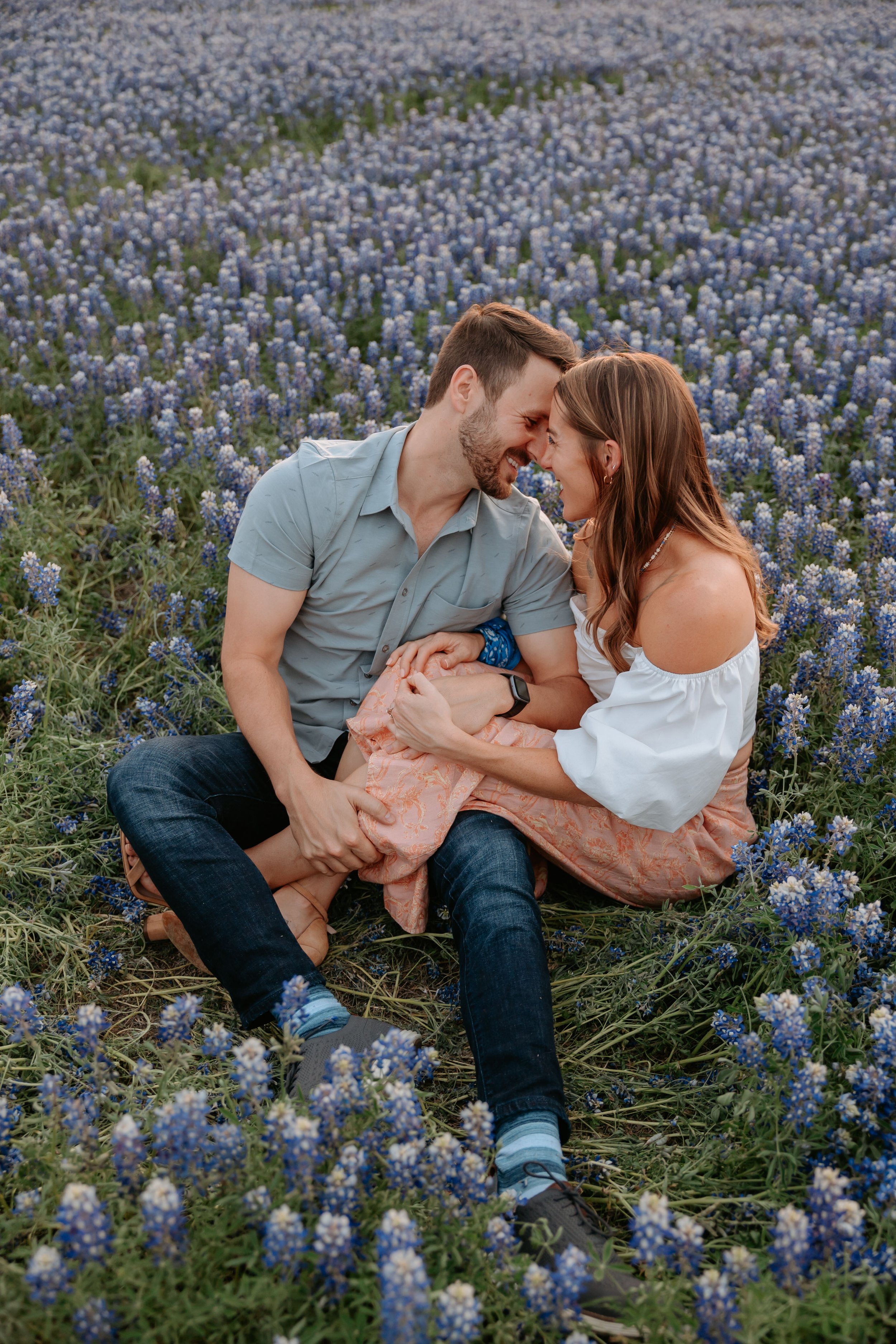 Man and woman sit a field of blue flowers.