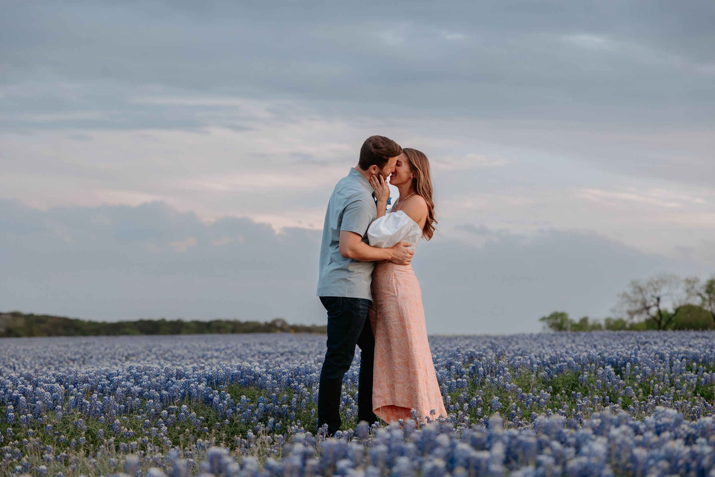 Man and woman kiss in a field of blue flowers.