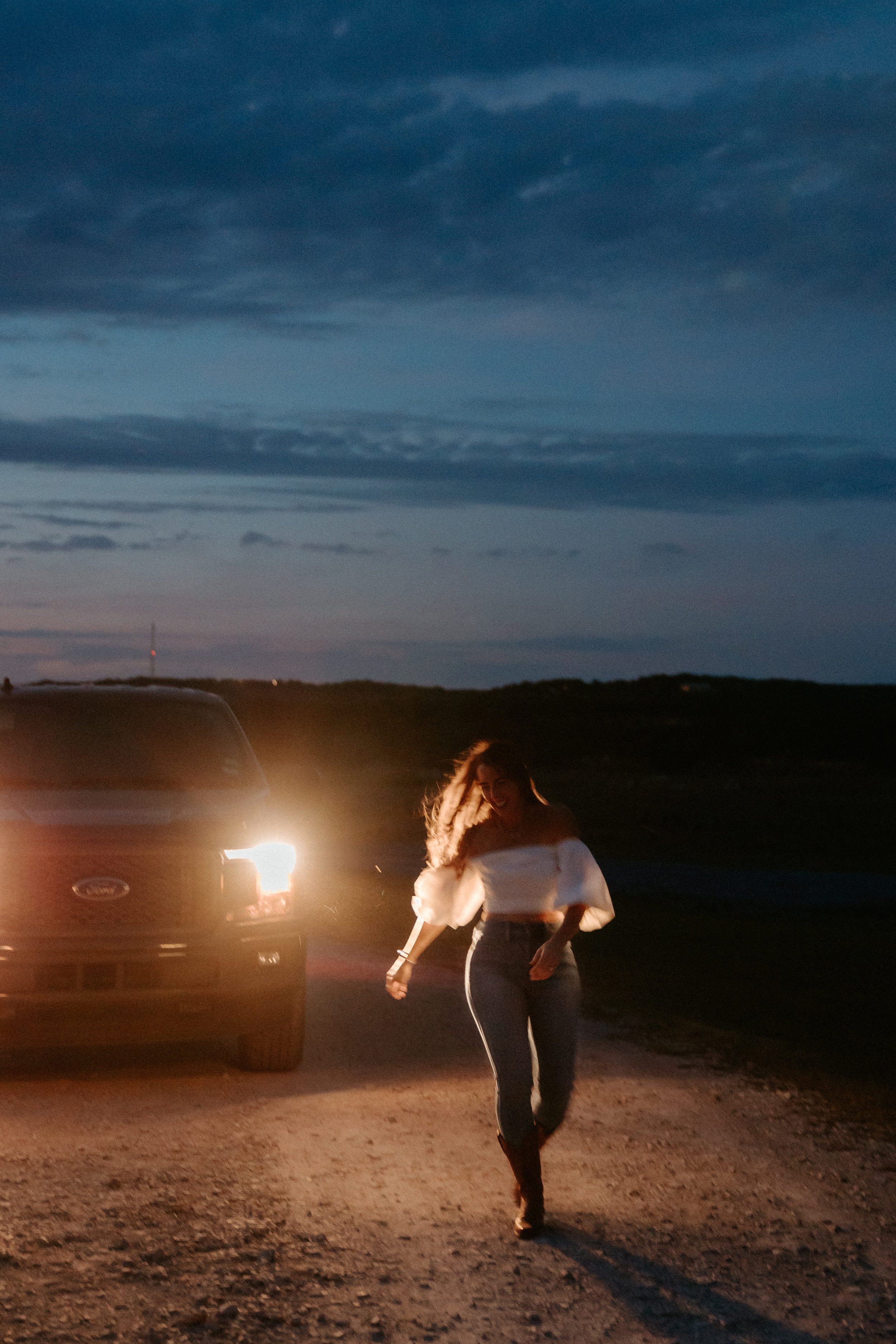 Woman dances with truck headlights in background.