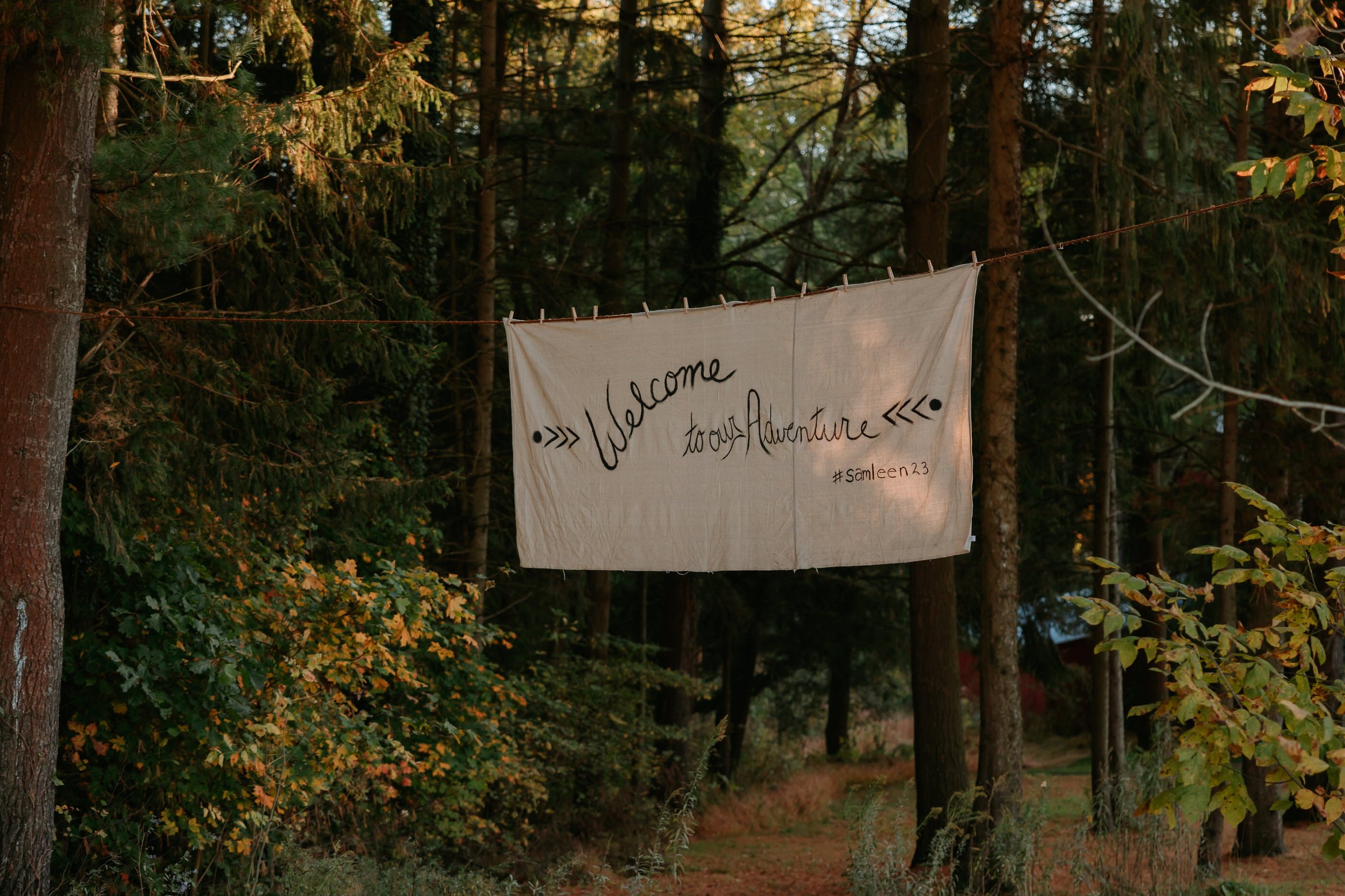A brown wedding sign hangs in the trees.