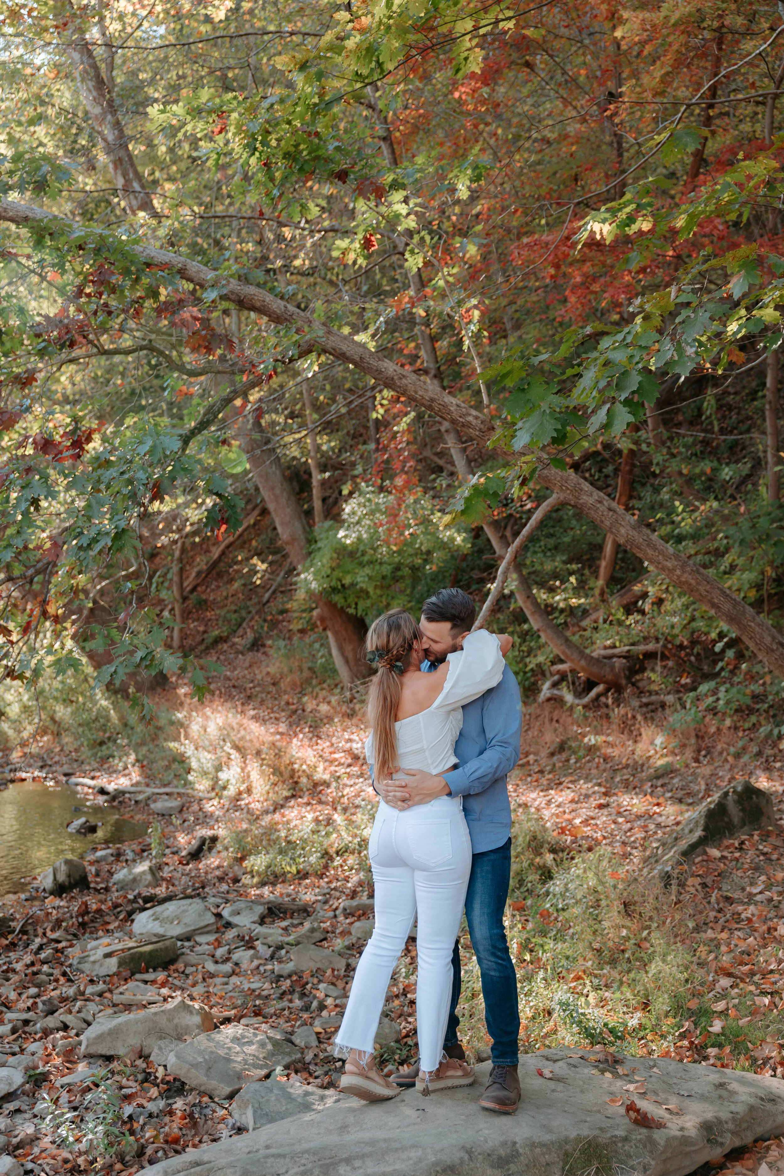 Man hugs woman while standing on large rock.