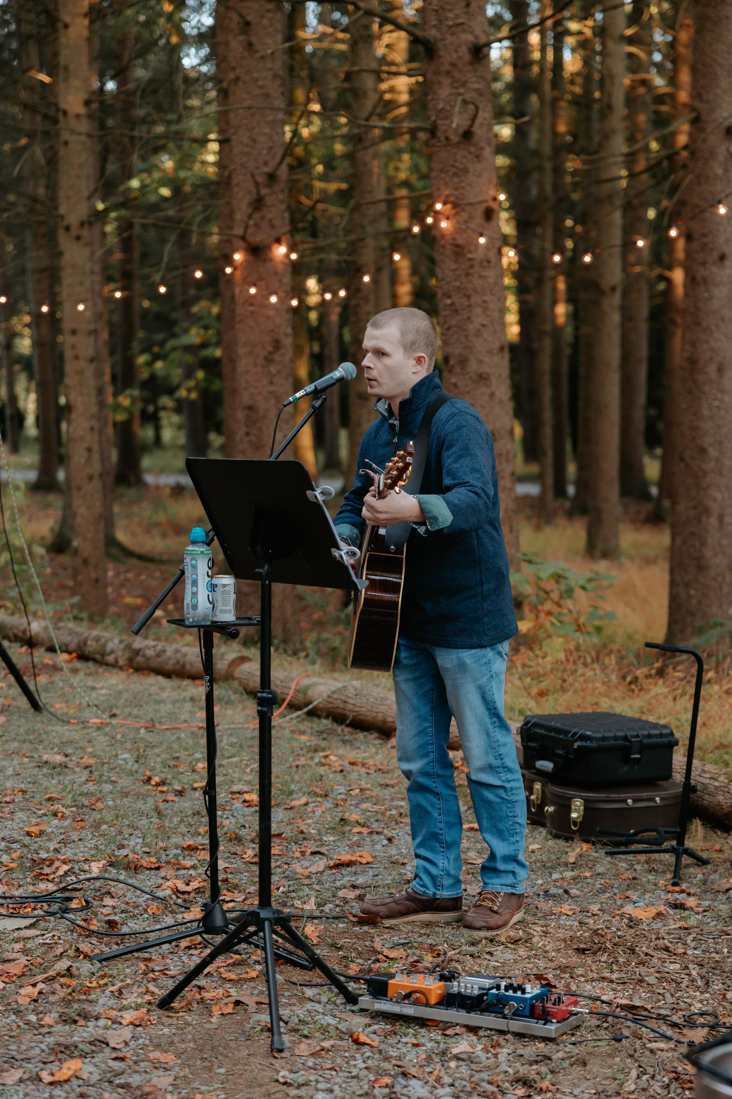 A man plays guitar in the woods.