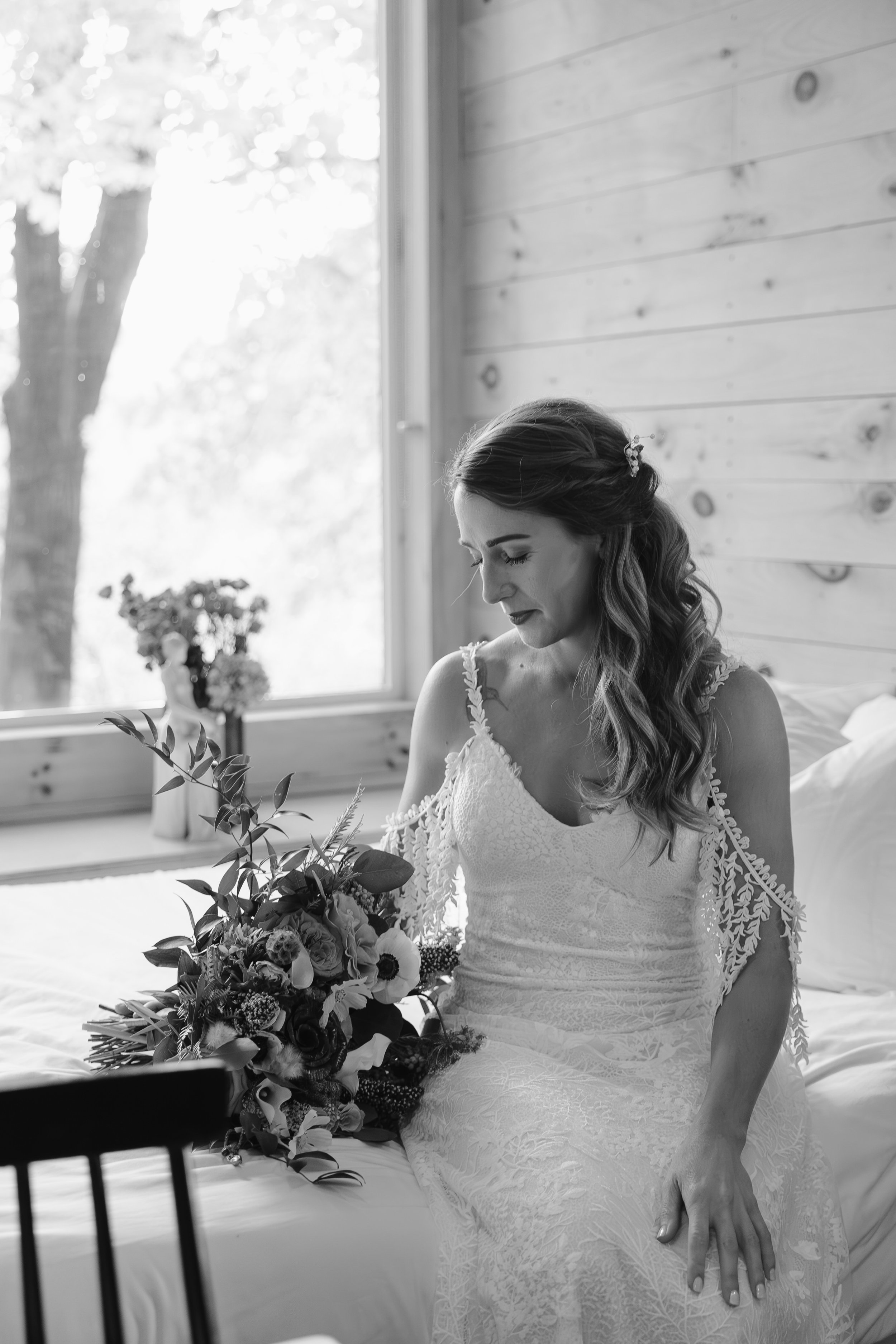 Bride sits on a bed looking at her flowers.