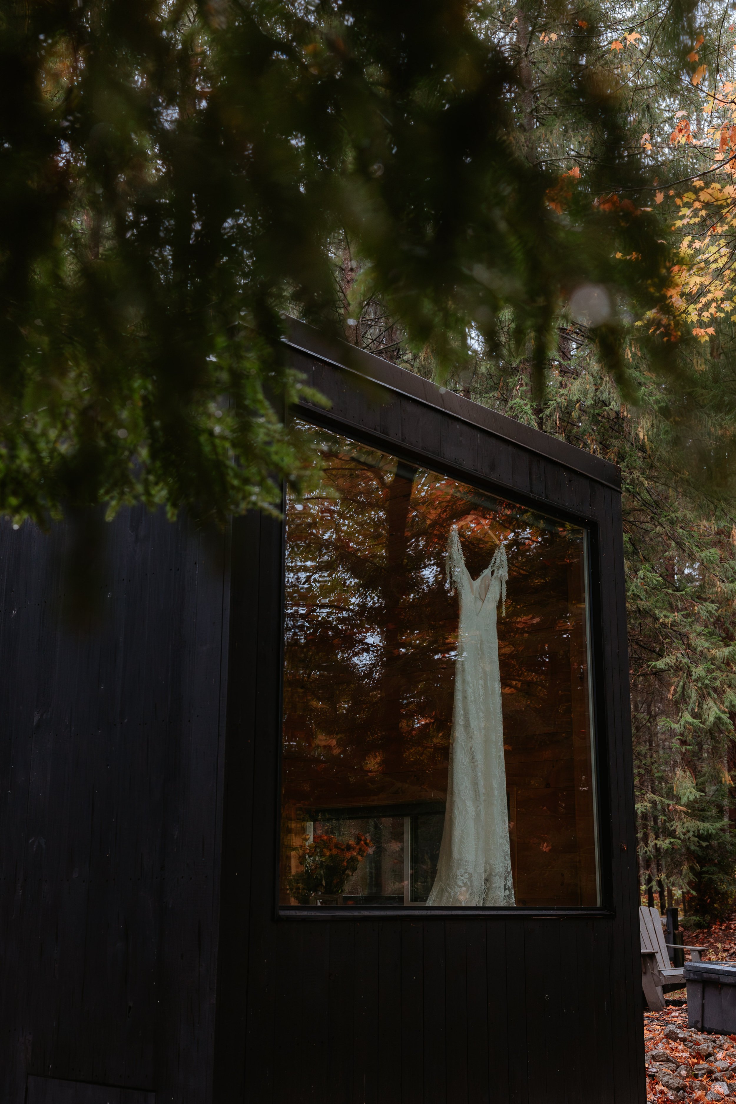 Wedding dress hangs in the window of a black cabin.
