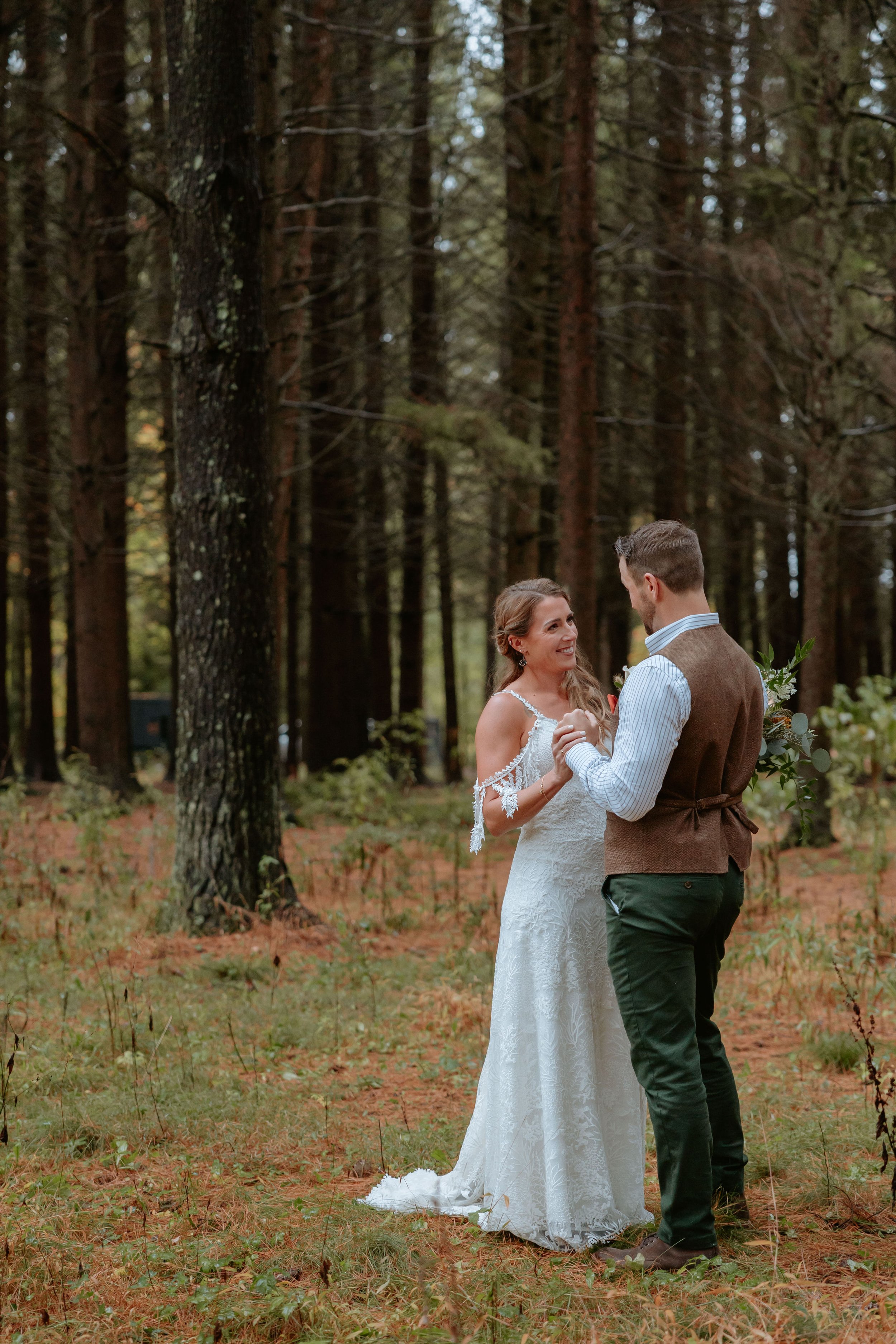 A bride and groom hold hands in a forest.