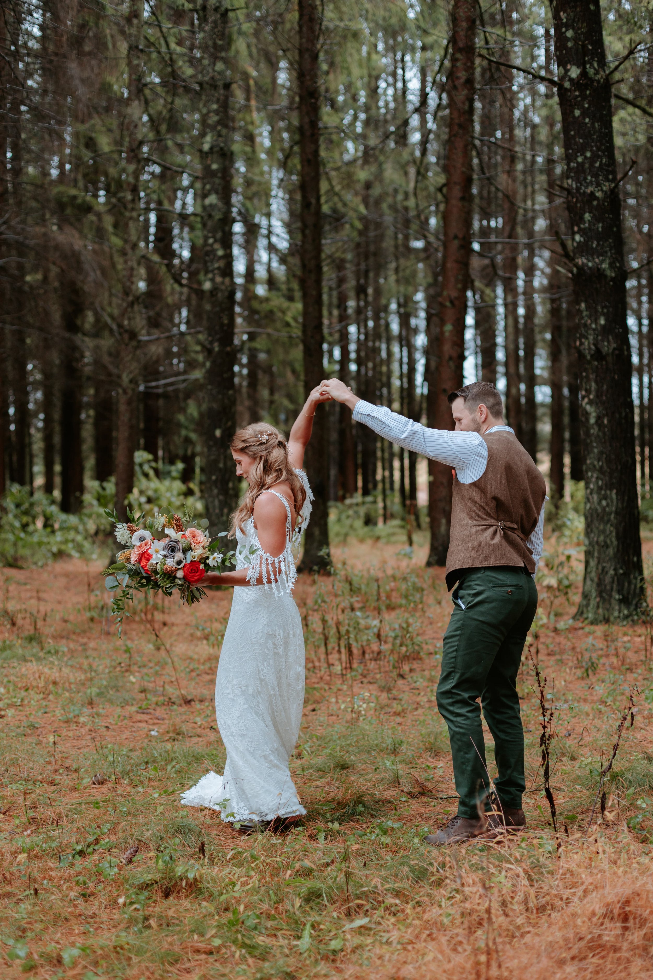 Groom twirls bride around in forest.