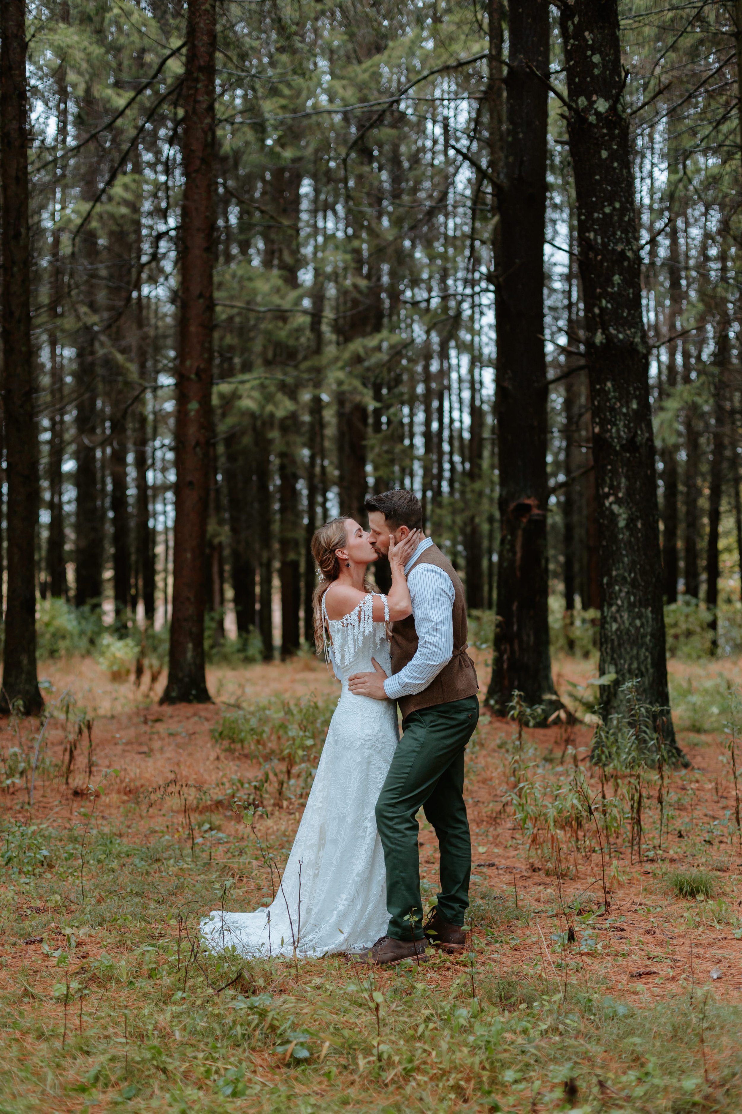Man and woman kiss in forest of pine trees.