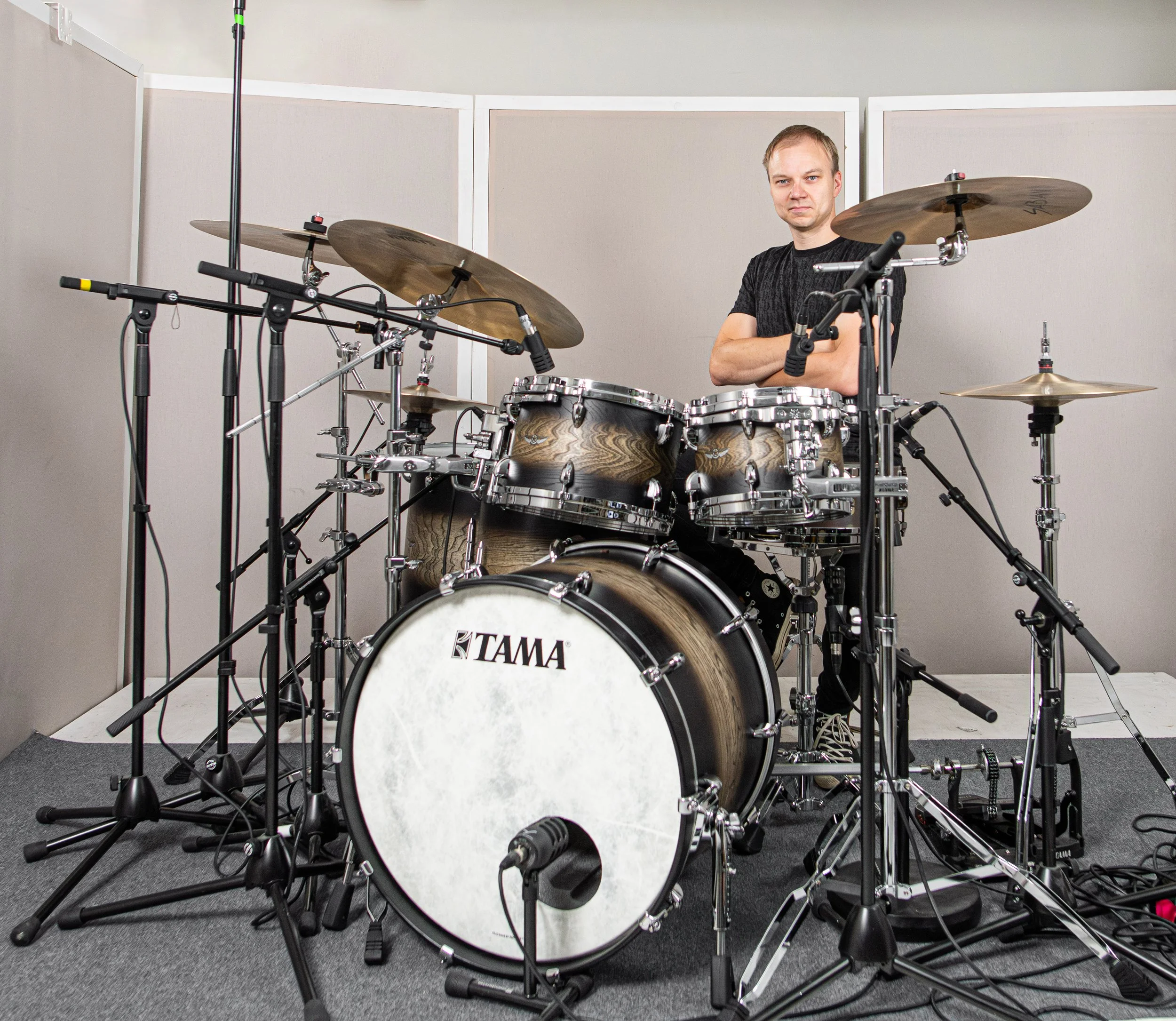 Tuomas Rauhala standing with crossed arms behind a large drum set in a recording studio.