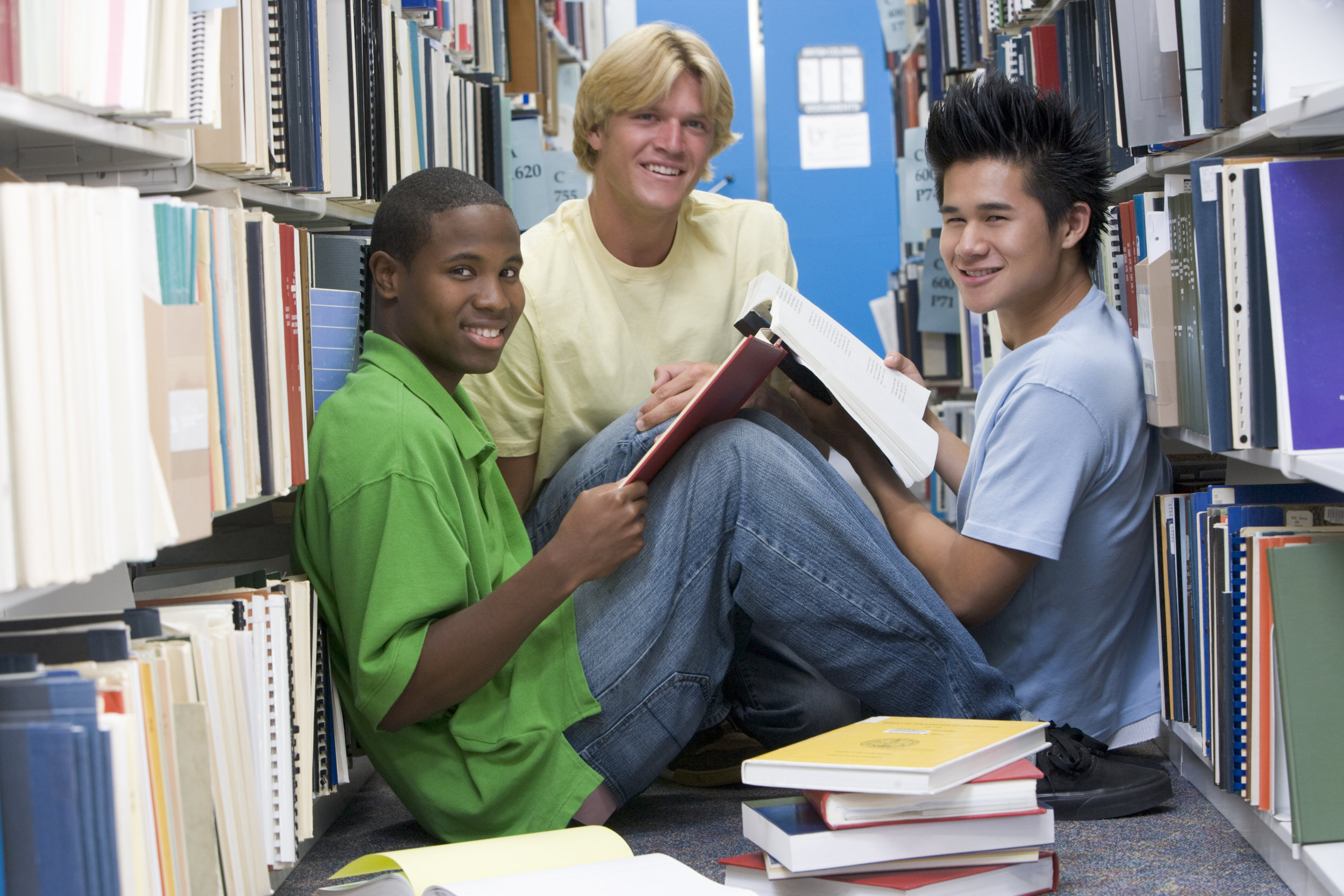 group-of-three-male-students-sitting-on-floor-of-library-surrounded-by-books_HFtNGBRSs.jpg