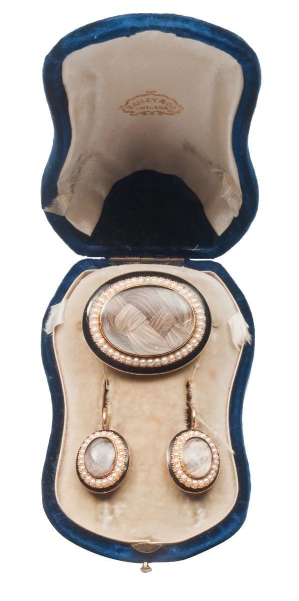 American mourning set in gold, black enamel and pearls in original box. Intricately woven hair is encased in glass; one earring is engraved EHH, the other JMH, December 15th, 1856