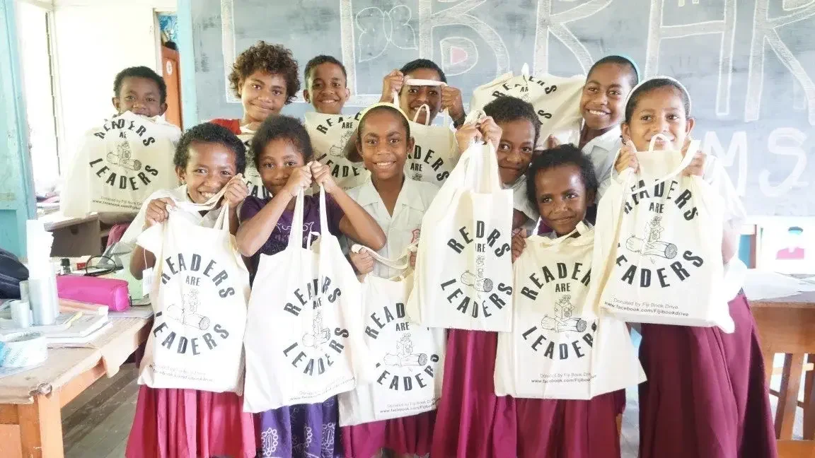 A group of smiling children holding Fiji Book Drive book bags.