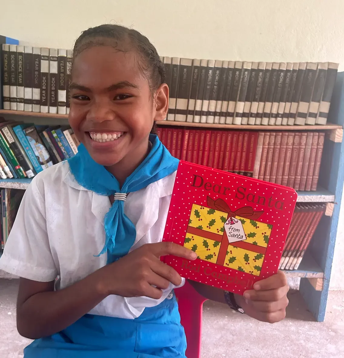 A young Fijian boy smiling and holding a book.