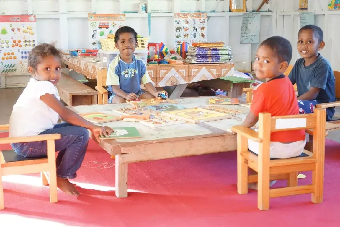 Four Fijian children sitting around a table engaging with books and puzzles.