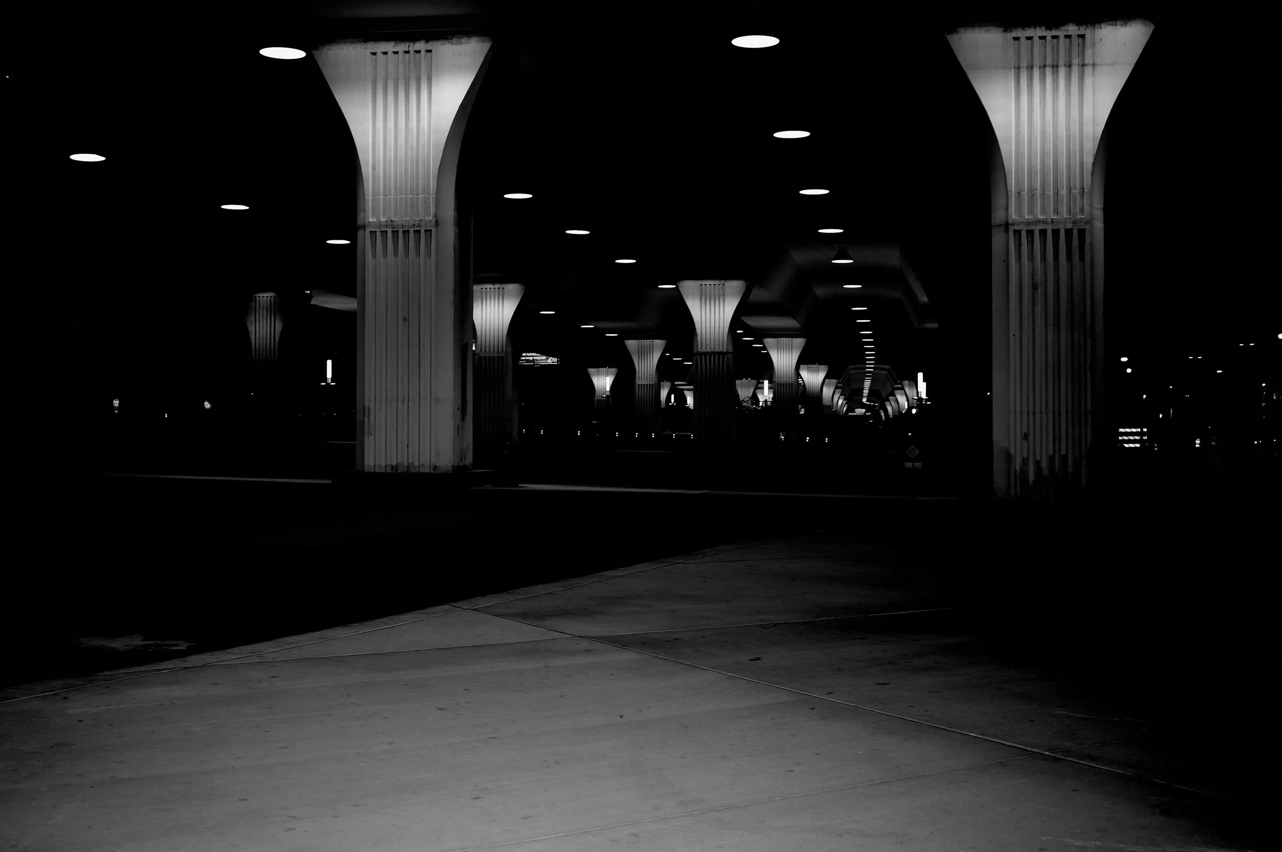 Black-and-white photograph of illuminated columns beneath the interstate at City Walk BHAM near the BJCC in Birmingham, Alabama, by Nathon Ruehl.