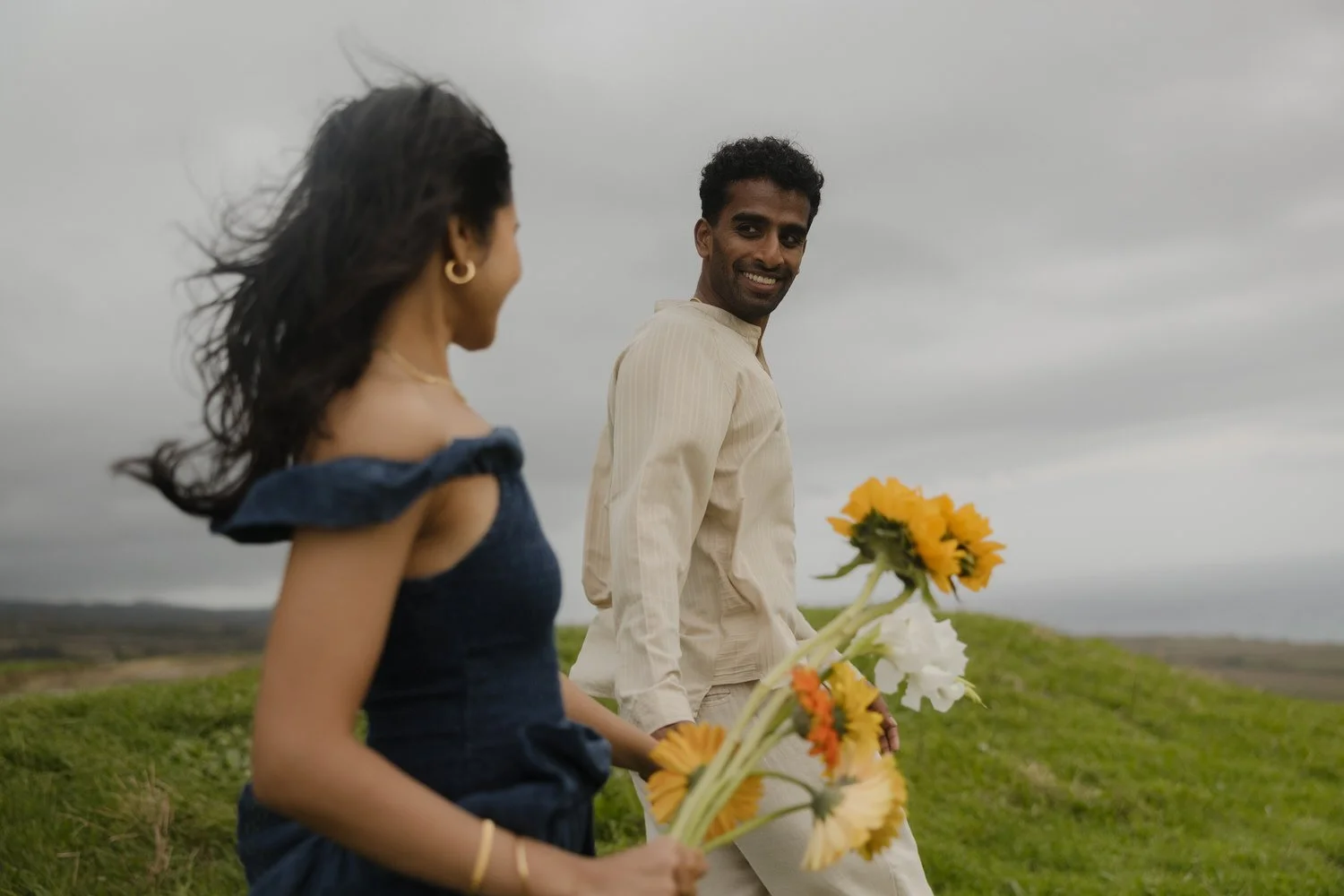 Couple walking with flowers through green hills of São Miguel Azores during engagement session