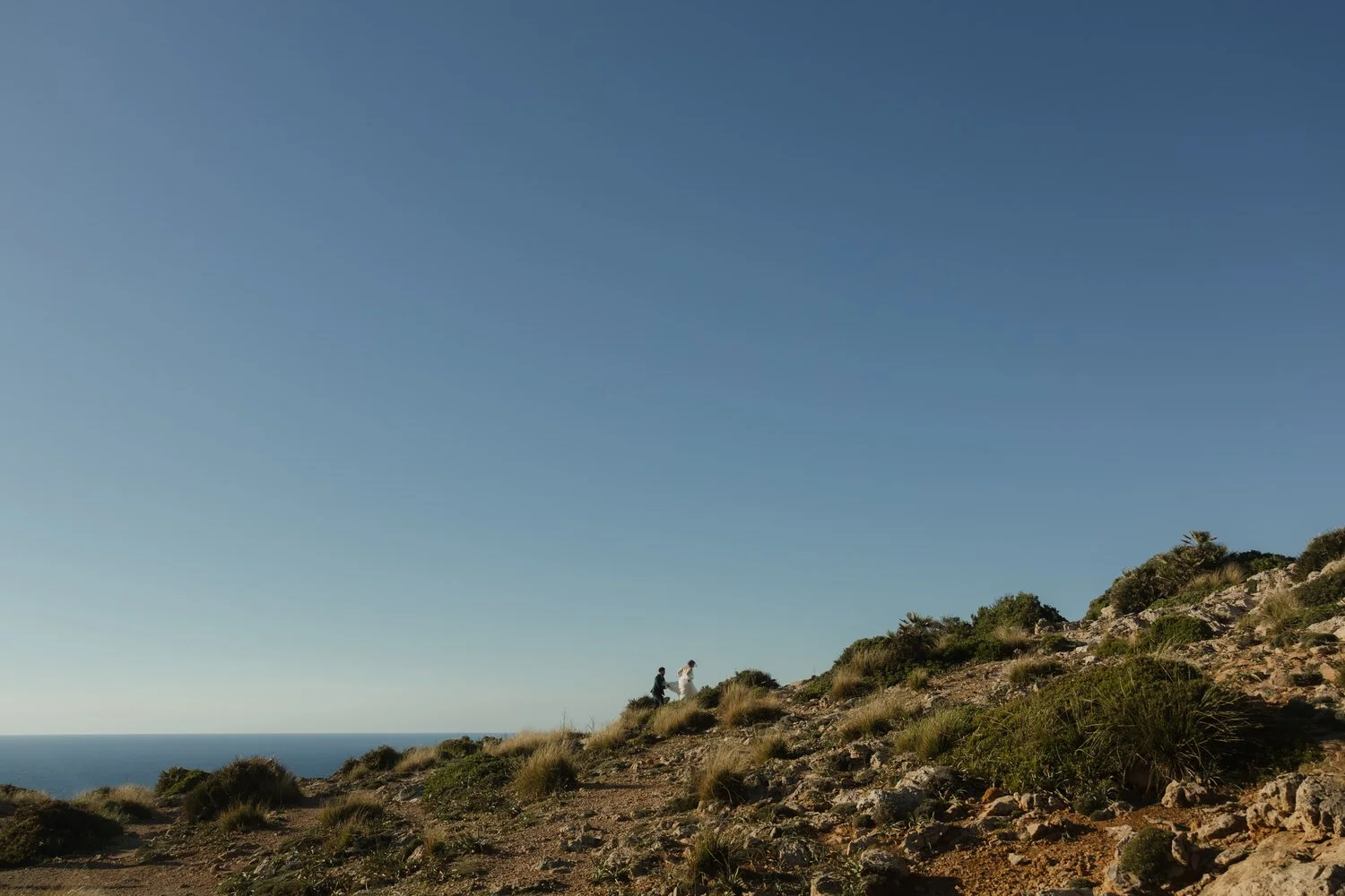 Bride and groom hiking through the rugged landscape of Cap de Formentor during their Mallorca elopement adventure.