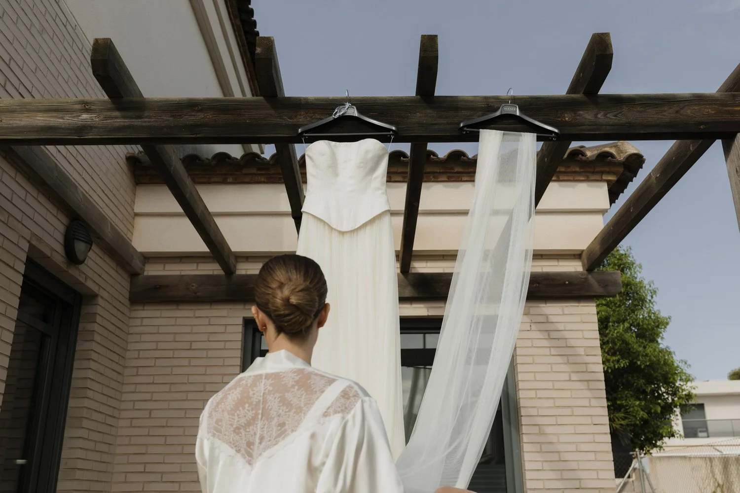 Bride during wedding preparations, looking at her dress and veil hanging outside her family home near Valencia