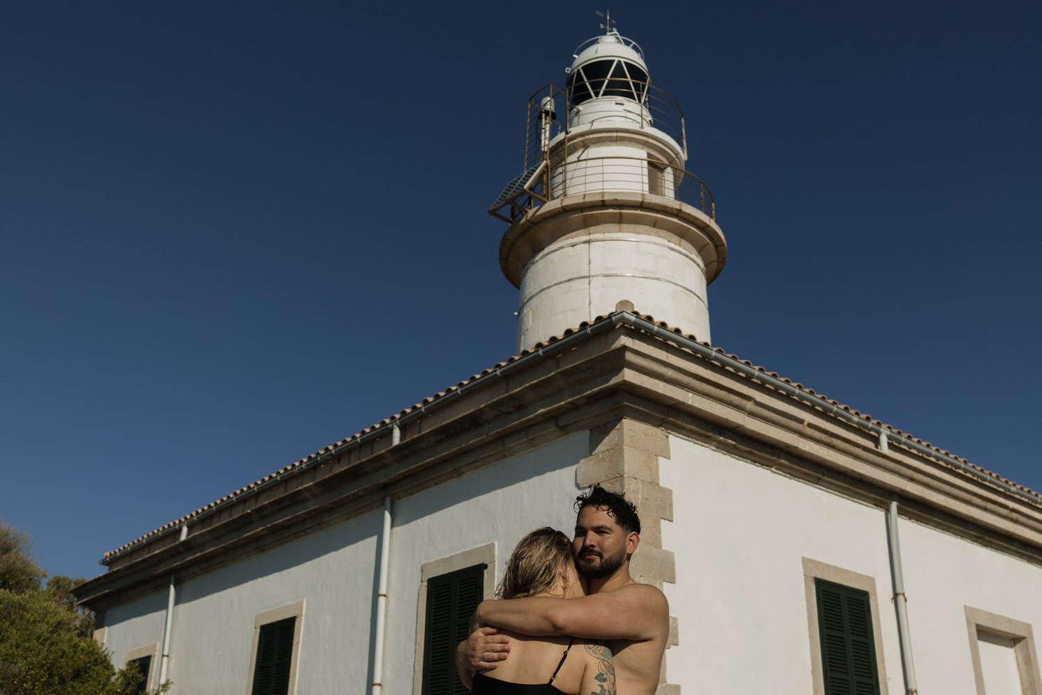 Couple embracing beside a lighthouse during a Mallorca sunrise experience.