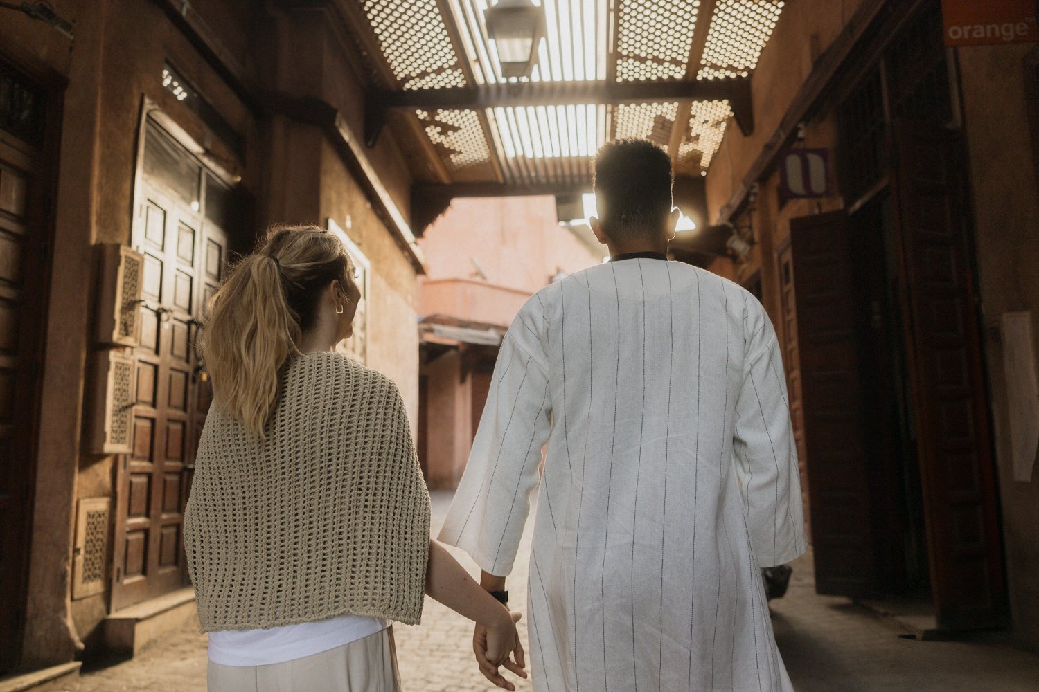 Couple walking hand in hand through a sunlit alley in Marrakech’s medina before their Beldi Country Club wedding