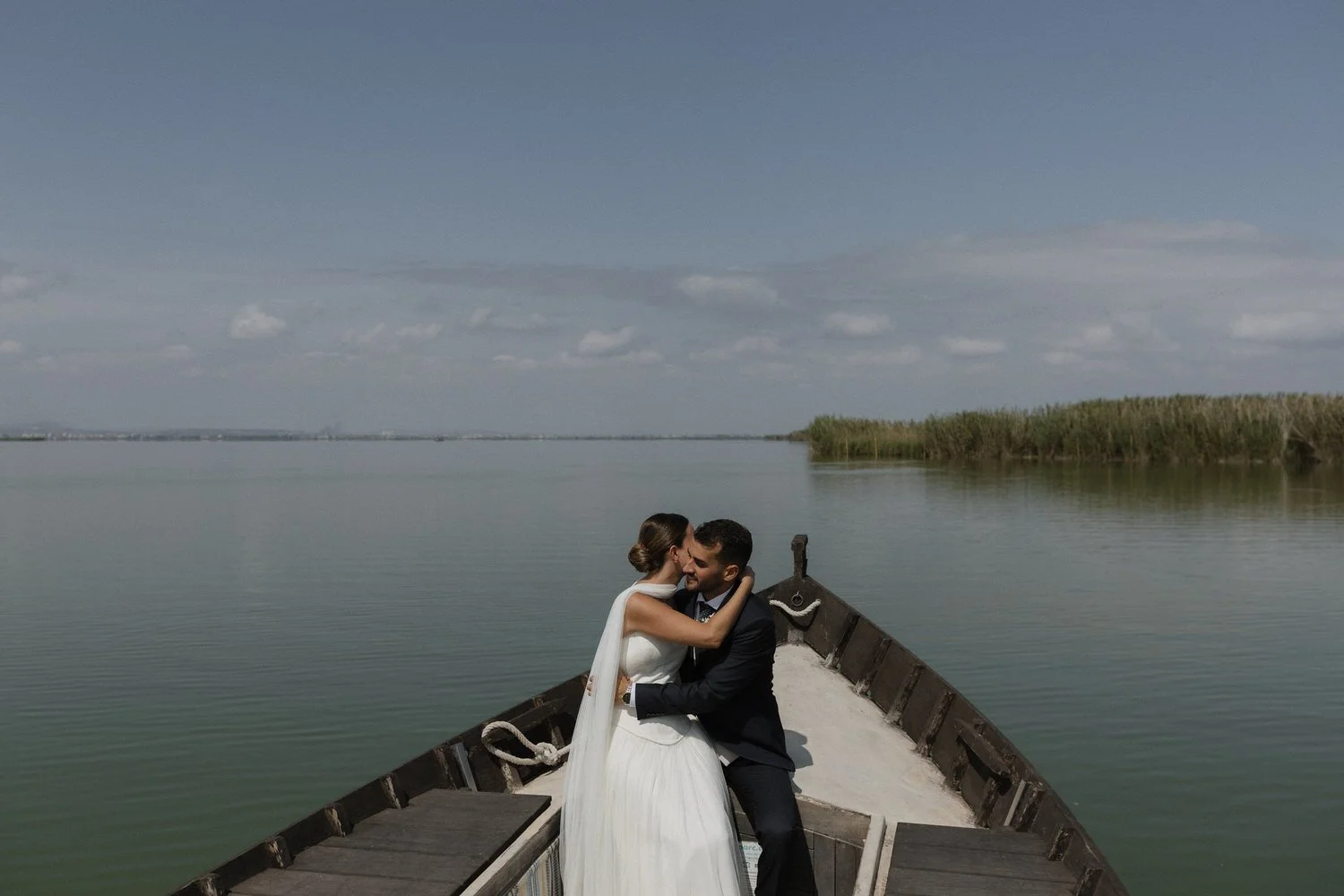 Bride and groom embracing on a traditional boat surrounded by the calm waters of the Albufera