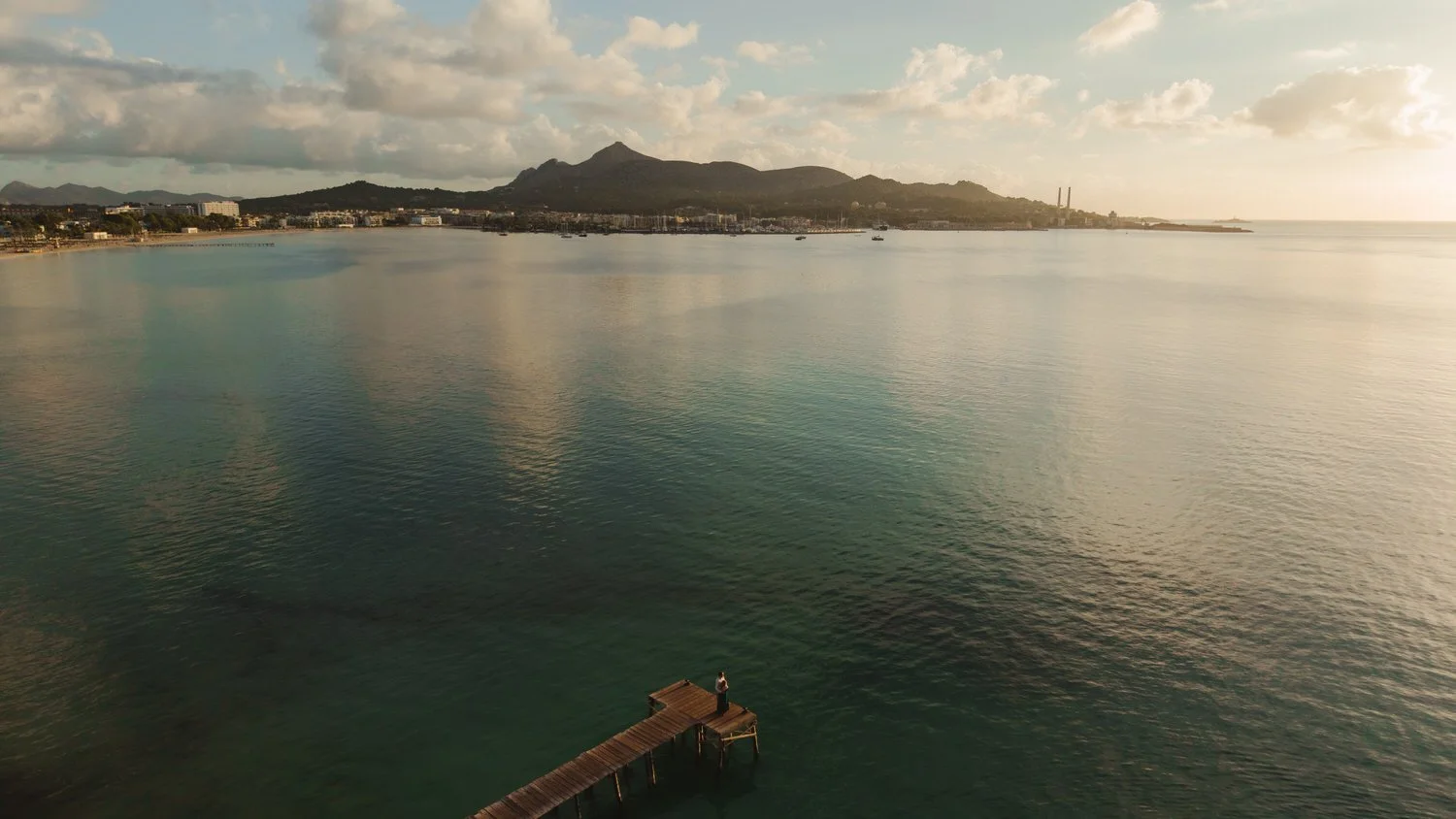 Drone photo of a couple on a wooden pier during their Mallorca elopement at sunrise, with the coastline and mountains in the background.