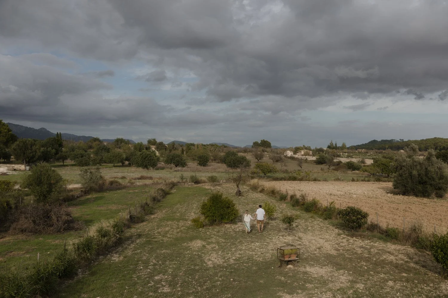 Couple walking through a rustic countryside villa in Mallorca during their elopement morning, surrounded by dramatic clouds and serene landscape