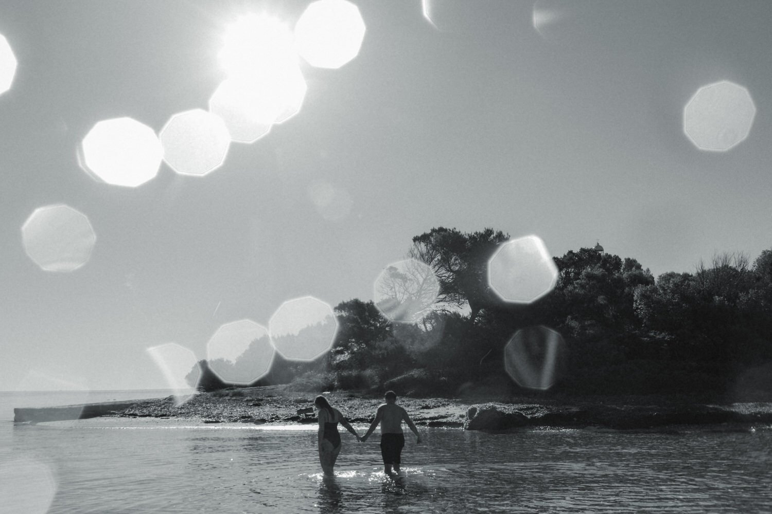 Couple walking through the water towards a lighthouse in Mallorca at sunrise.