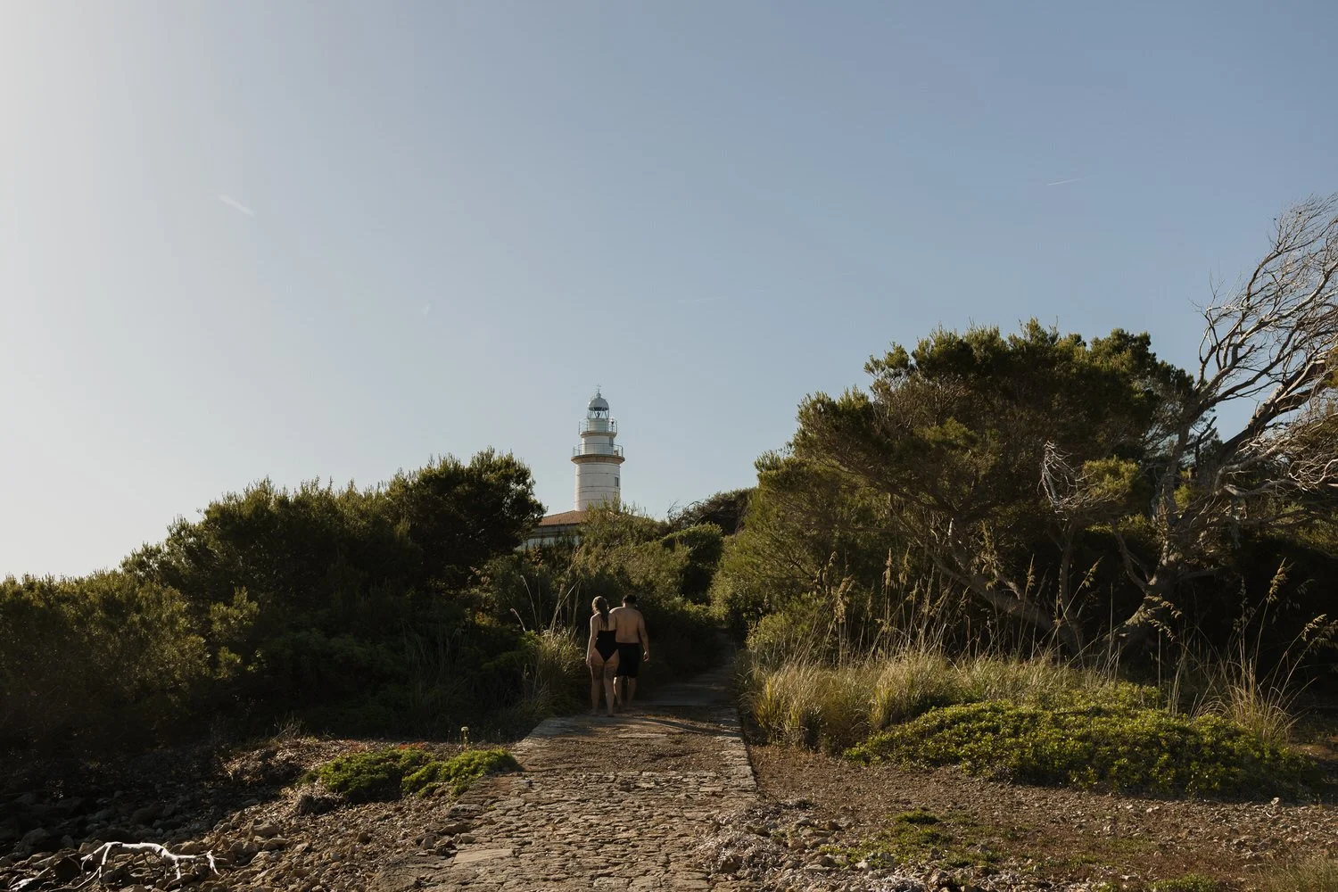 Couple walking towards the lighthouse during a sunrise experience in Mallorca.