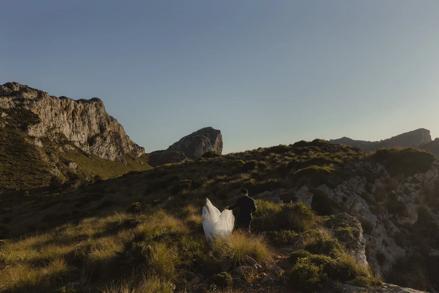 Bride and groom walking through the rocky landscape of Cap de Formentor during a sunset elopement in Mallorca.