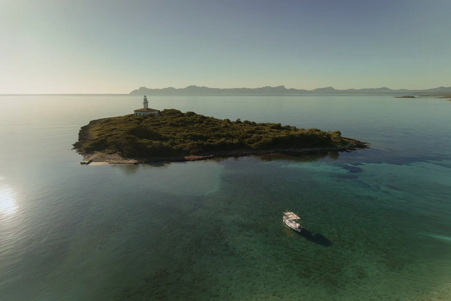 Boat anchored beside a lighthouse in Mallorca during a sunrise elopement.