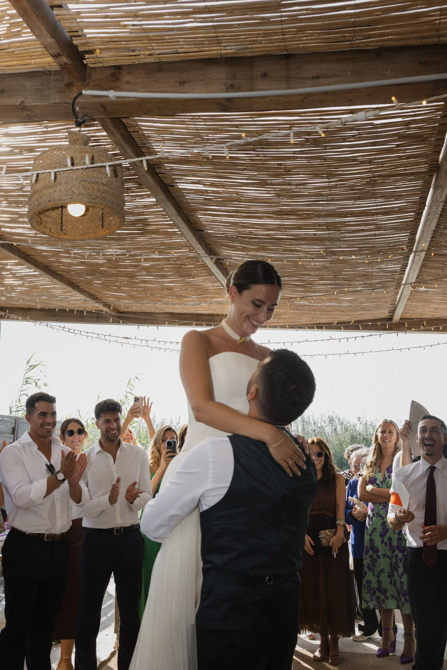 Bride and groom dancing together under a rustic wooden canopy, surrounded by guests celebrating and clapping at a traditional wedding in El Palmar, Valencia.