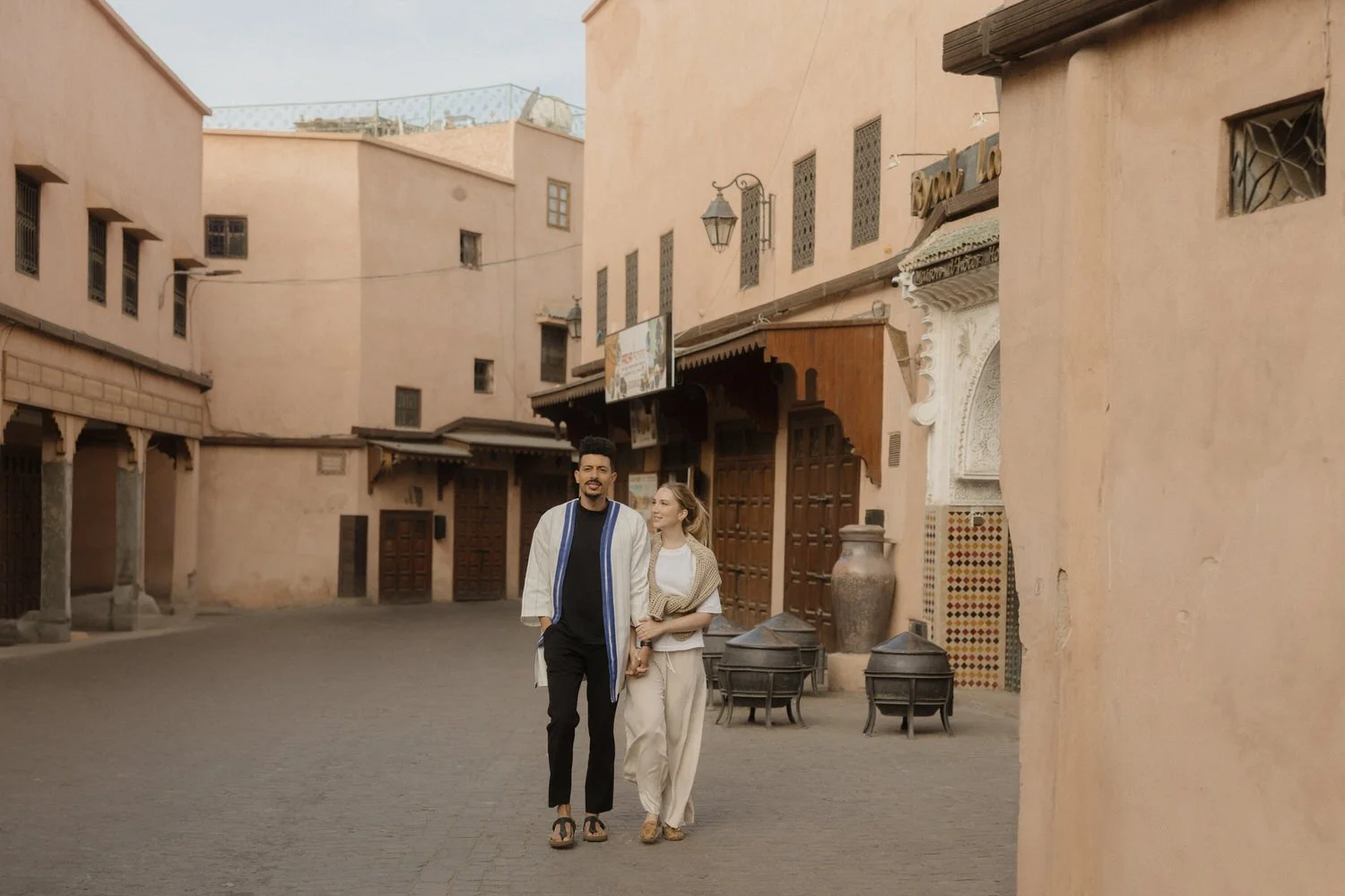 Katie and Amine walking together through a quiet street in Marrakech during their destination wedding weekend, surrounded by warm terracotta walls and traditional Moroccan architecture.