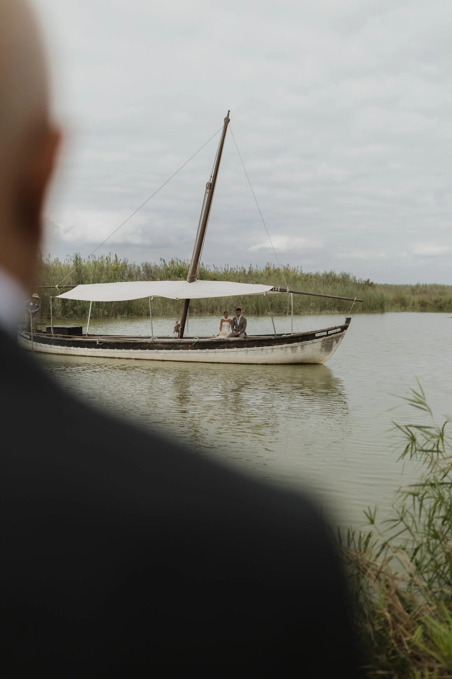 Bride arriving by traditional boat across the Albufera as her father waits on the shore at La Barraca del Palmar