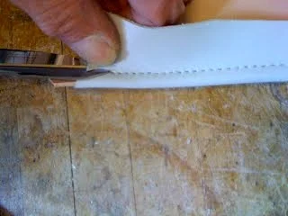 Using sharp, thin scissors you can cut off excess leather near the stitch line. This method avoids the undesired shallow cut left in the base material when removing excess leather with an exacto blade.