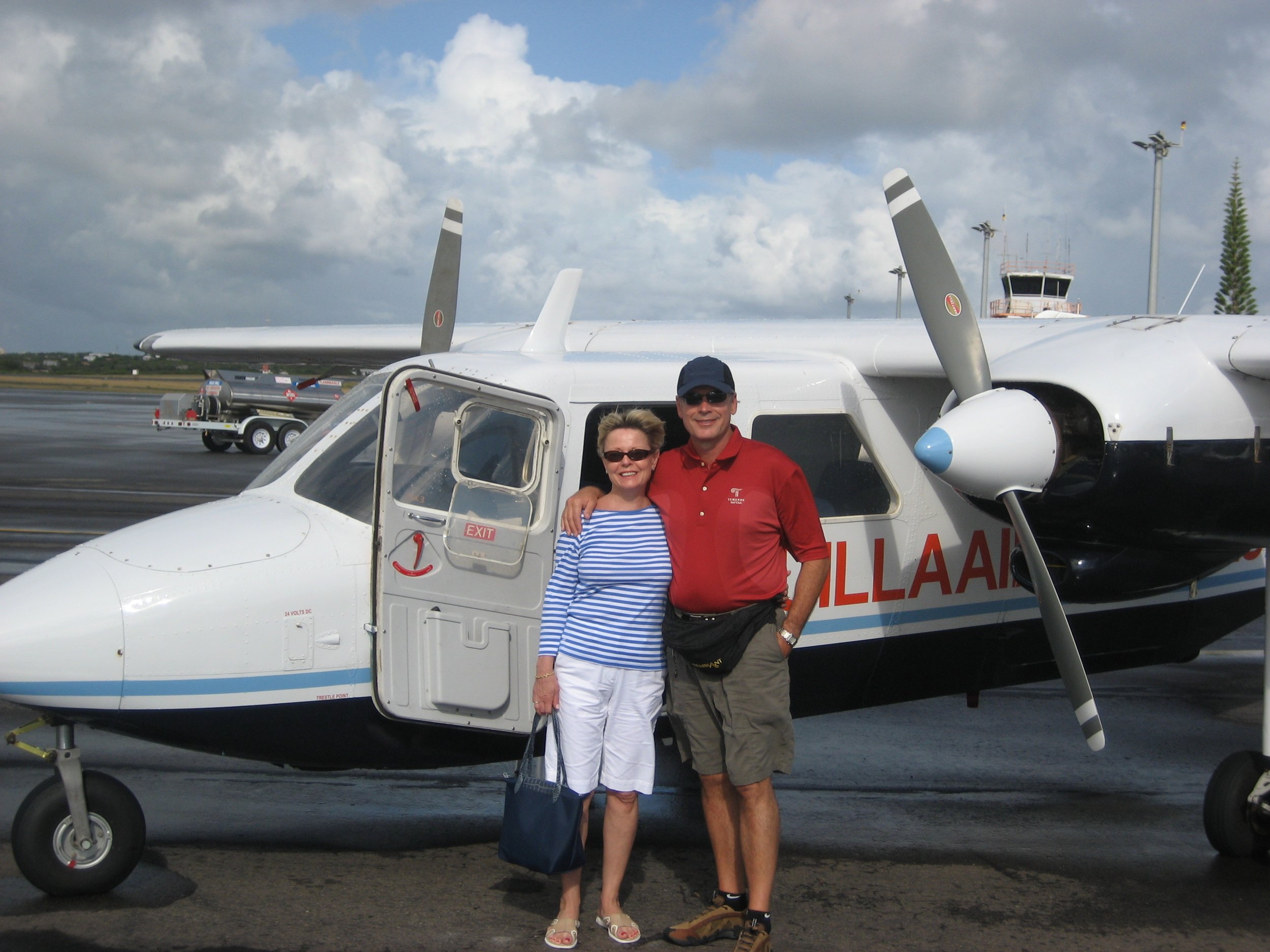 John & Lynn Weber are standing in front of a small white airplane getting ready to fly to St. Barts, on an airport tarmac.