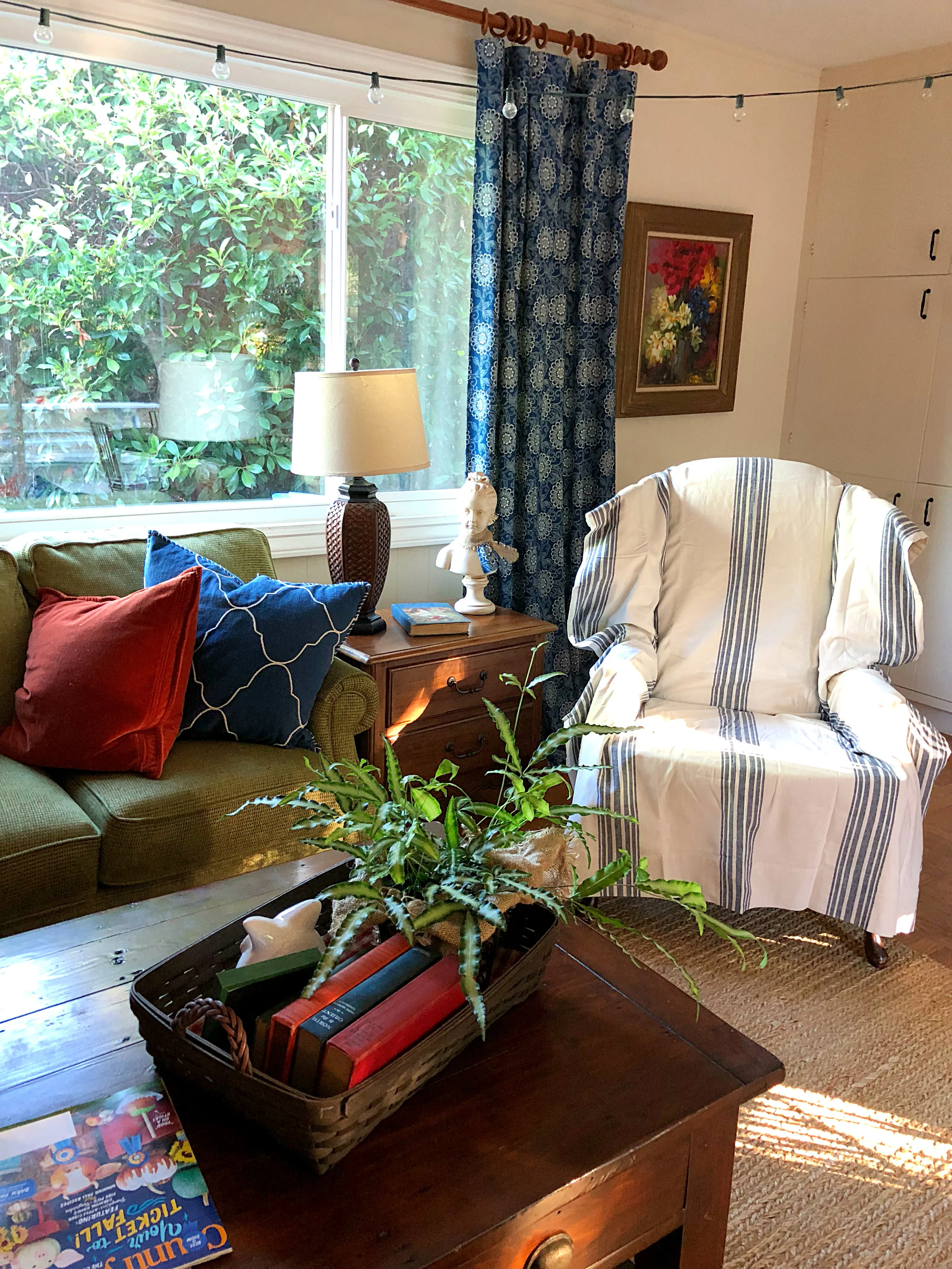 A few touches of Fall color change this room with the season. The striped chair is a roadside find with a PB curtain over it. Curtains - calico corners fabric sewn by a friend, end table, lamp, bust - consignment, oil painting by my grandmother, sofa - Flexsteel, pillows, rug and coffee table - Pottery Barn, string lights because we don’t have overhead lighting.