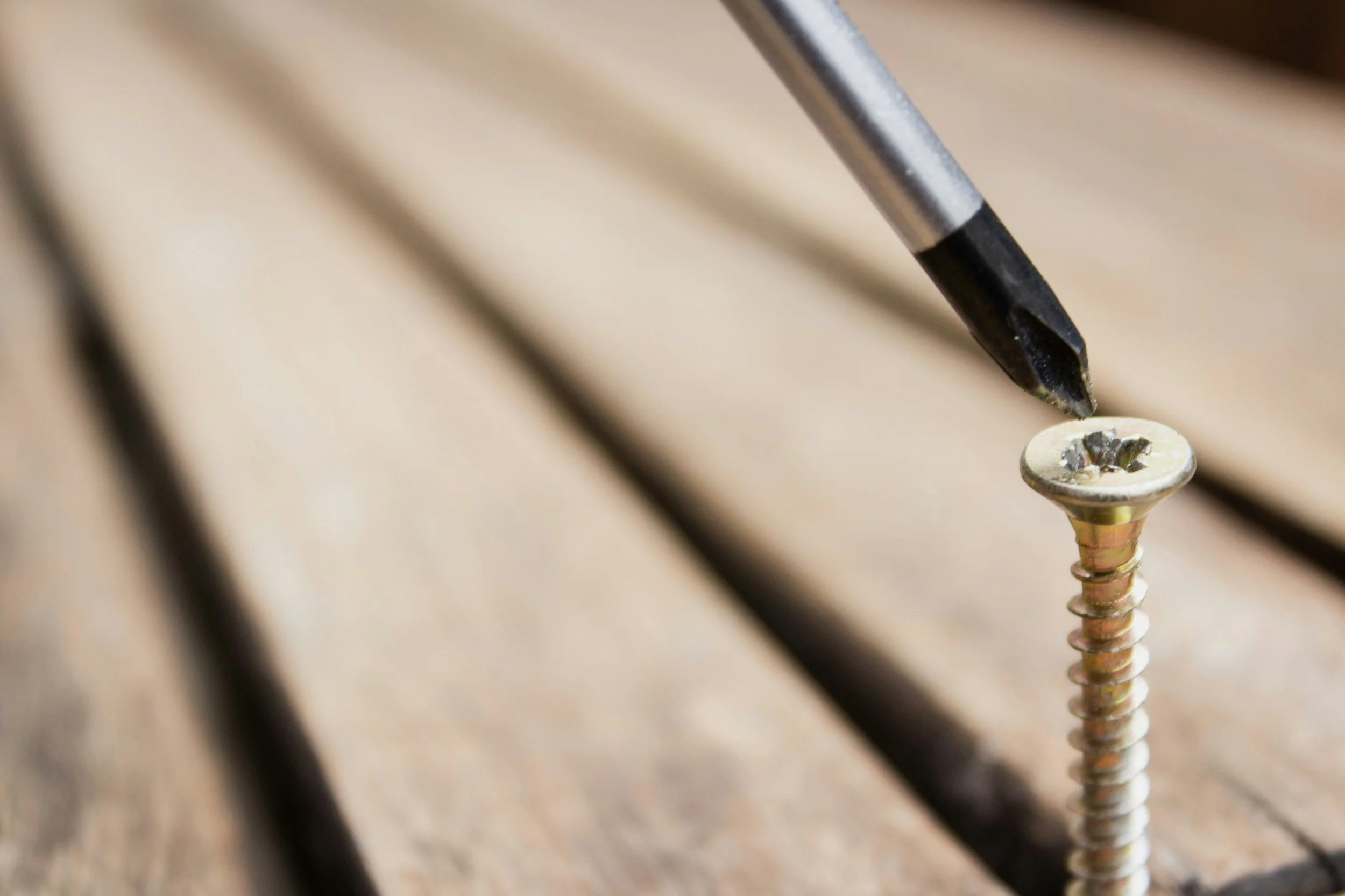Close-up of a black screwdriver tip being used to tighten a gold-colored screw on a wooden surface.
