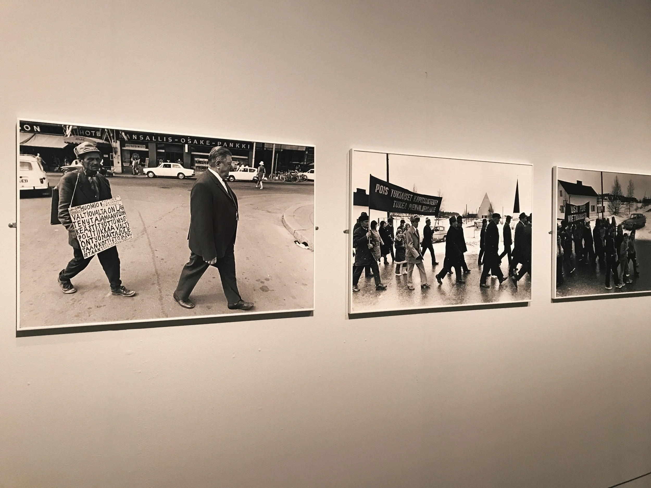 Kalervo Ojutkankaan valokuvat osoittavat, että 1970-luvulla Suomessa marssittiin esimerkksi kapitalismia vastaan. Seuraavalla seinällä Saana Wang tarkastelee puolestaan nykyhetkeä ja suomalaisen yhteiskunnan tulevaisuutta muun muassa Rajat kiinni -mielenosoituksen kautta.