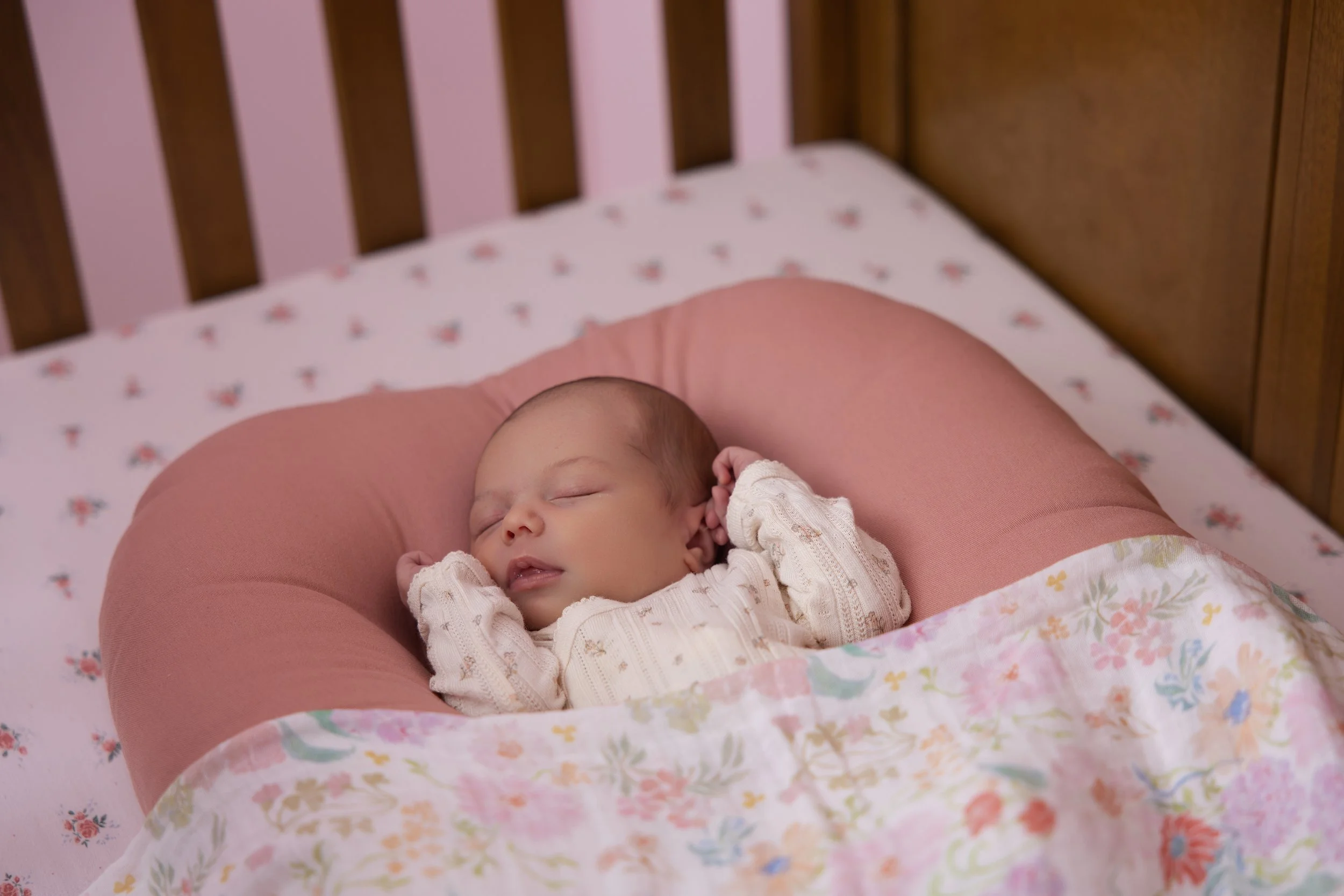 newborn baby wearing pink sleeping in her crib