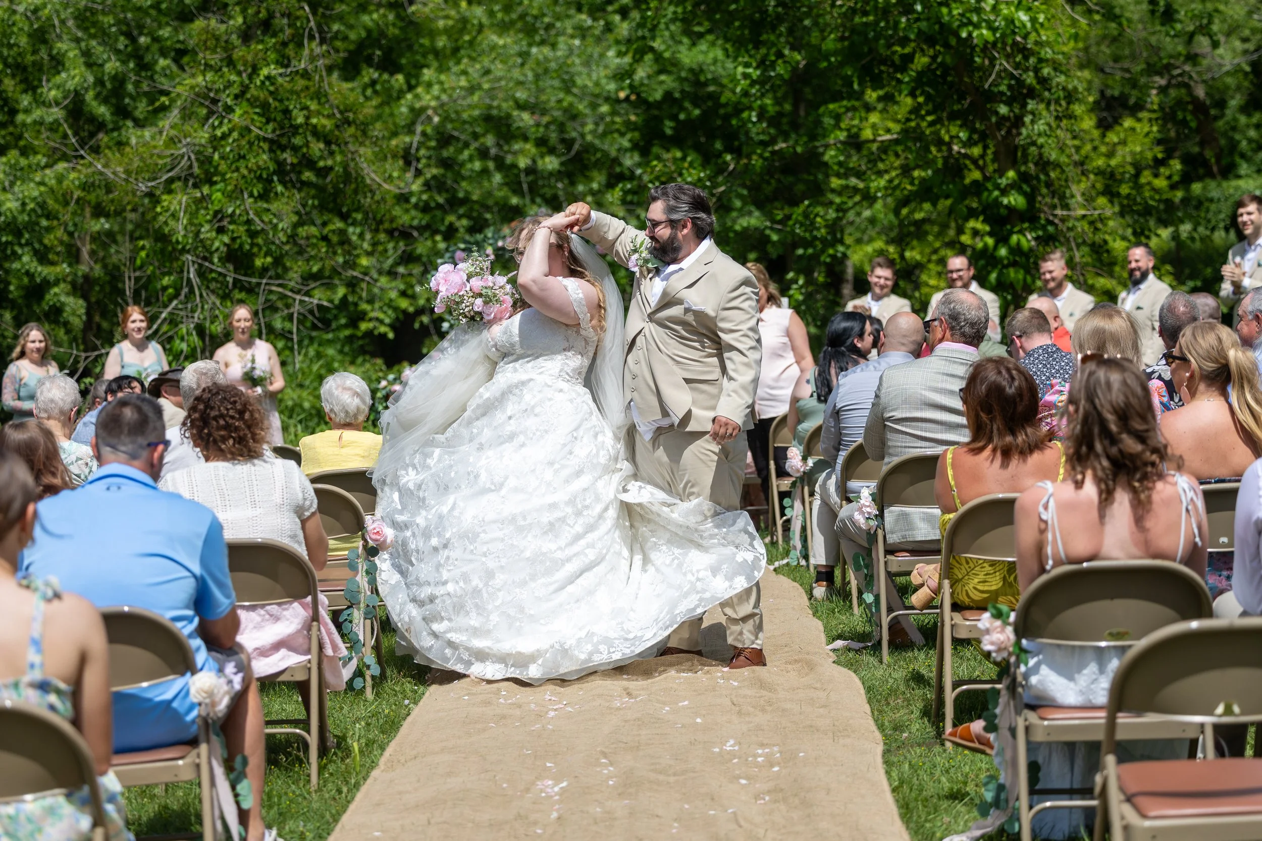 Bride and groom twirl on their wedding aisle after getting married with guest surrounding them on either side in chairs.