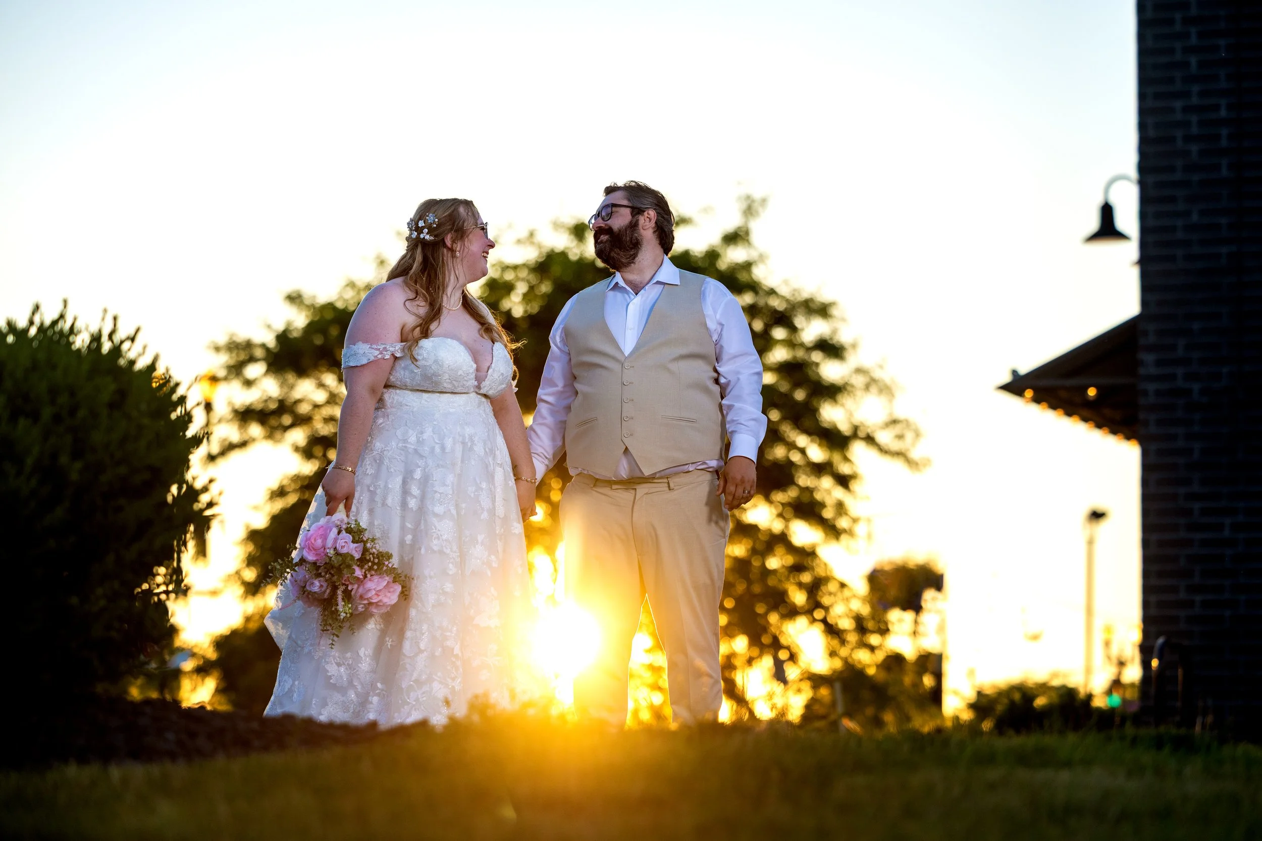 Bride and groom smile at one another at the end of their wedding day in front of sunset
